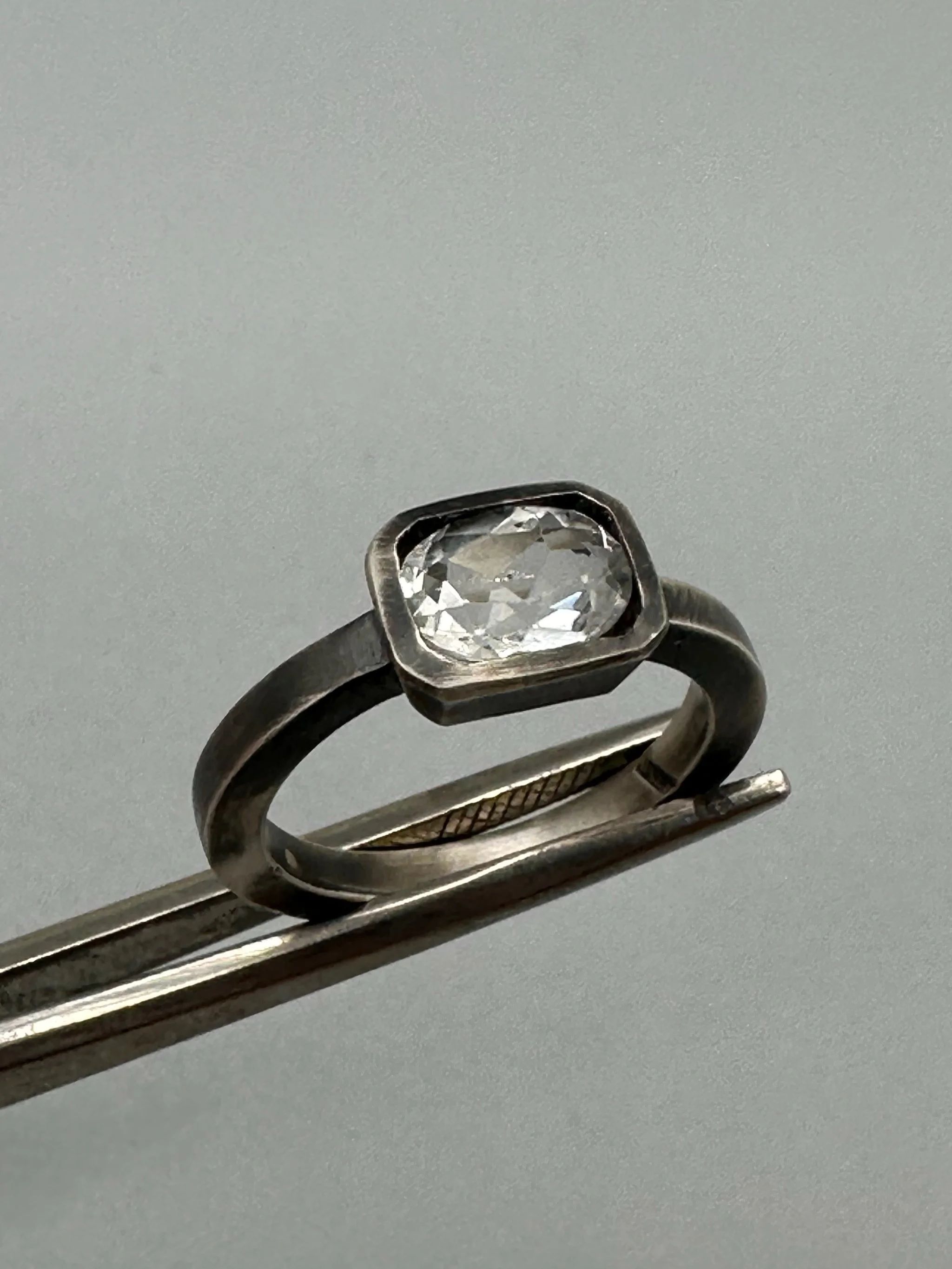 Anello White in Black in argento brunito con topazio bianco sfaccettato e castone geometrico. White in Black ring in oxidized sterling silver with faceted white topaz and geometric setting.
