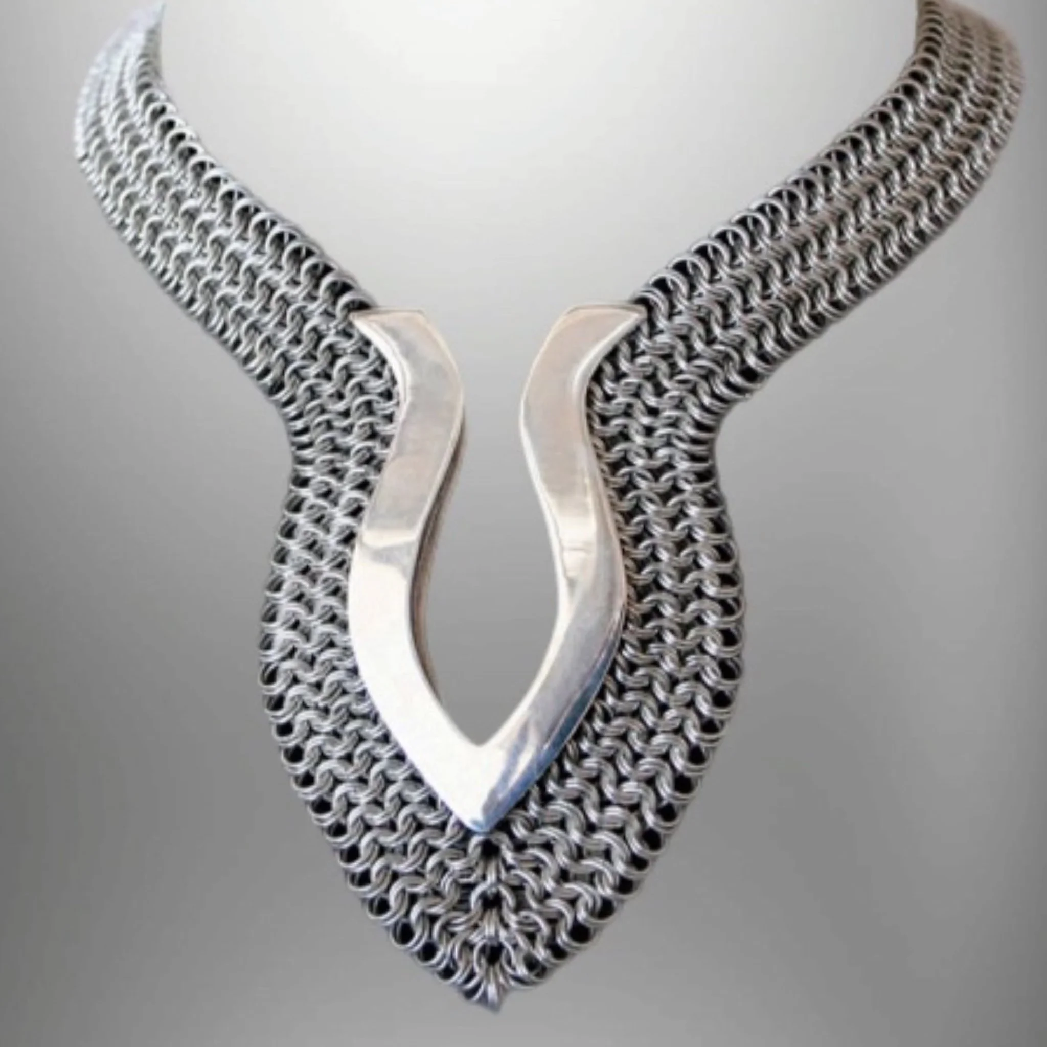 Collana e pendente di gioielli in metallo con un design intrecciato e un grande cuore argentato al centro.