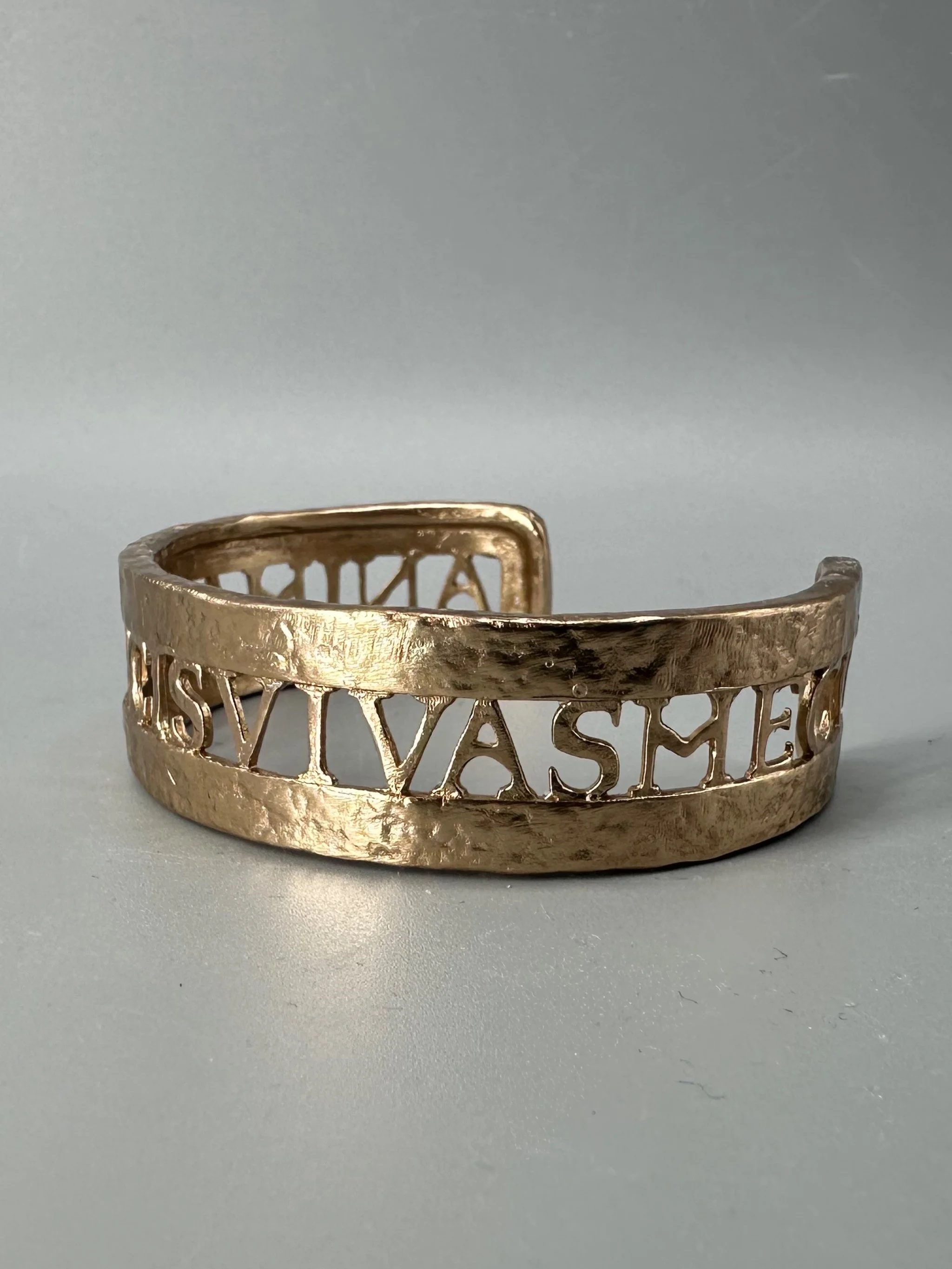 Bracciale Anima Dulcis di CōDICEDS in bronzo bocciardato, aperto e regolabile, con iscrizione latina traforata.  CōDICEDS Anima Dulcis open adjustable cuff in hammered bronze with openwork Latin inscr