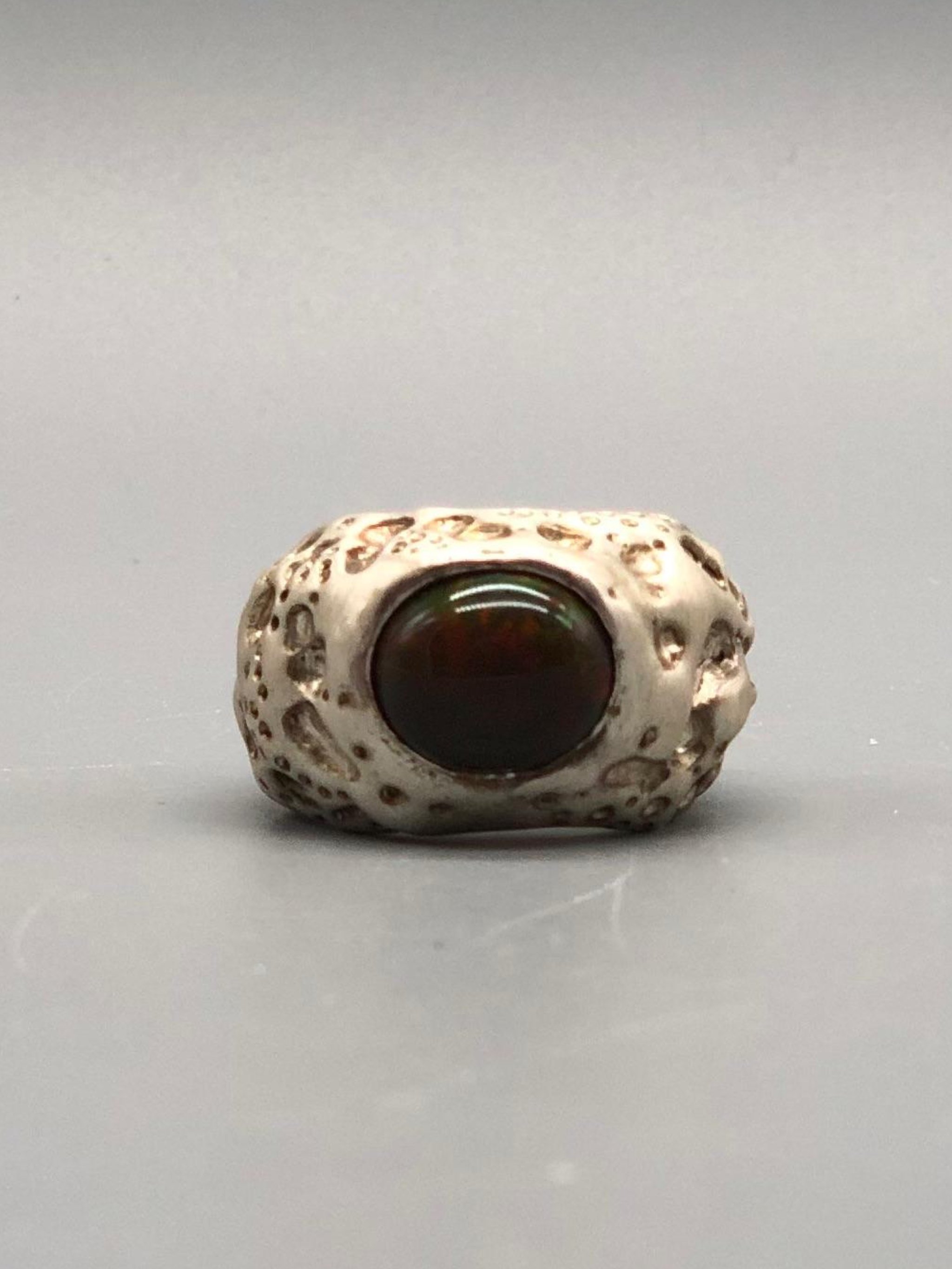 Luna ring by Portas Jewels in textured silver with a black opal showing deep red and green reflections.