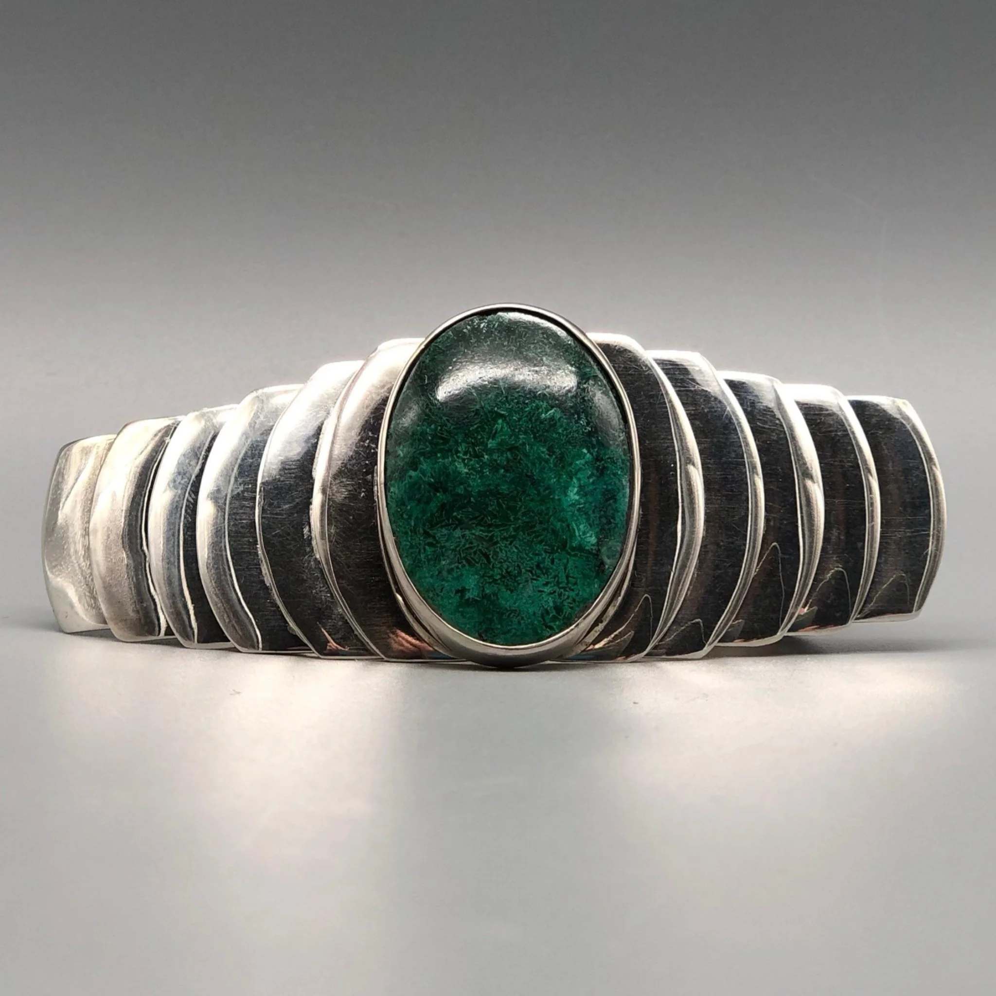 Bracciale in argento costruito per stratificazione, con un elemento centrale in crisocolla che definisce il punto focale.
La struttura si sviluppa per progressione, accompagnando la pietra in un equilibrio tra materia e ritmo.
Silver bracelet built t