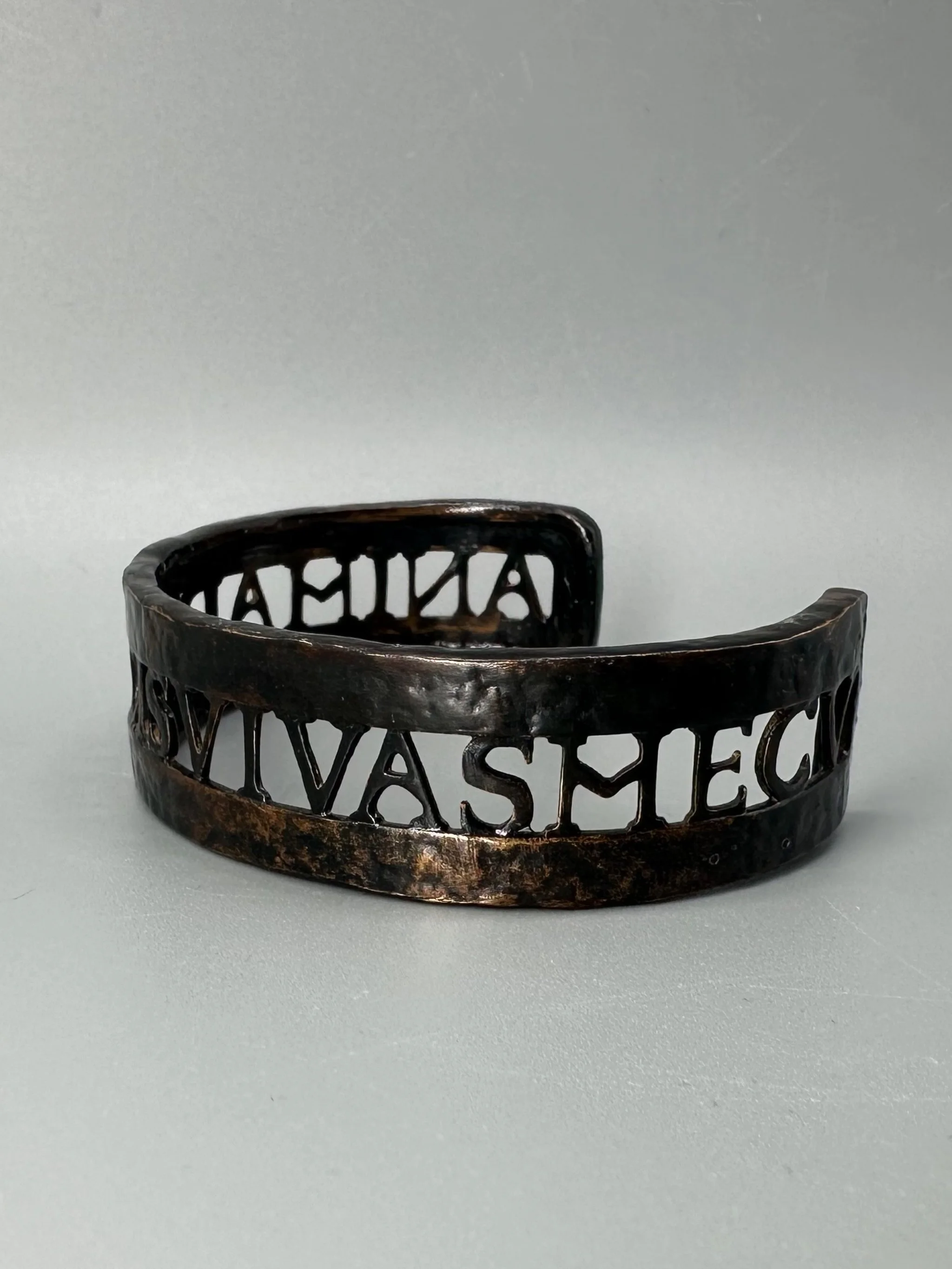 Bracciale Anima Dulcis di CōDICEDS in bronzo brunito, aperto e regolabile, con iscrizione latina traforata.  CōDICEDS Anima Dulcis open adjustable cuff in darkened bronze with openwork Latin inscripti