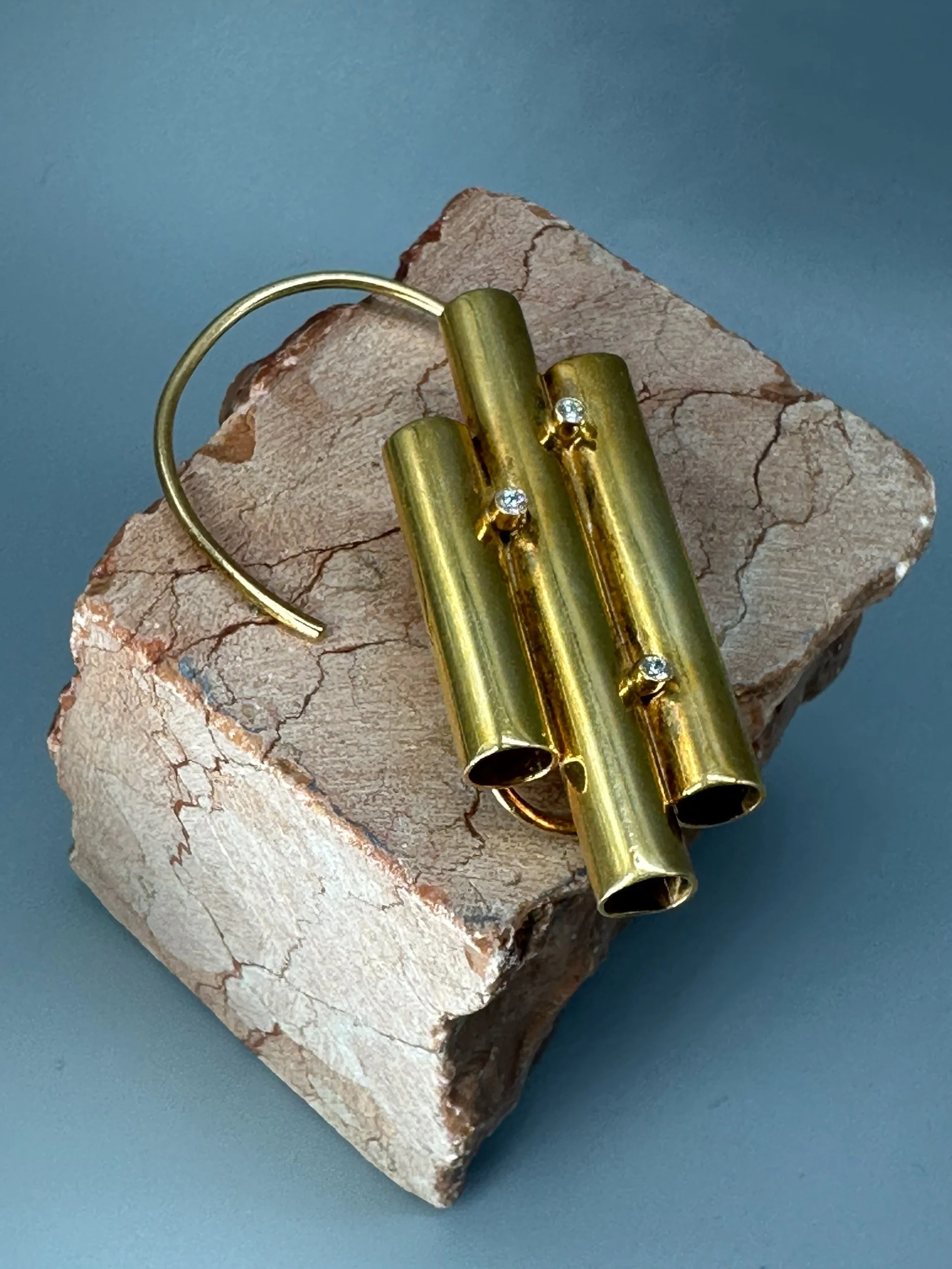The Earcuff di HoAsen, ear cuff dorato con cilindri asimmetrici. The Earcuff by HoAsen, gold-tone ear cuff with asymmetrical cylinders.