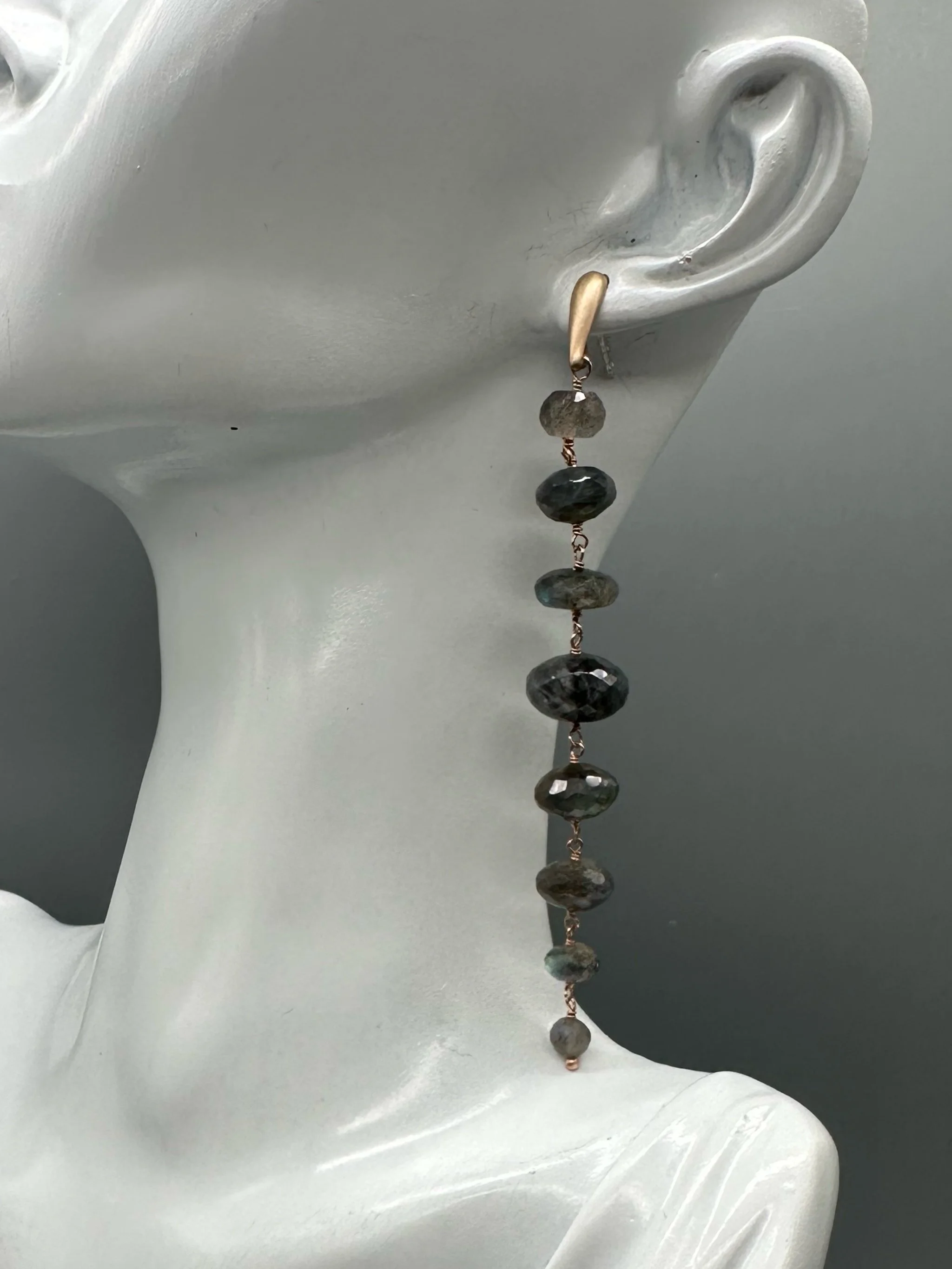 Orecchini Bold Labradorite con pietre grigie sfaccettate dai riflessi blu e verdi, disposte in verticale. Bold Labradorite earrings with vertically arranged faceted grey gemstones and blue-green refle
