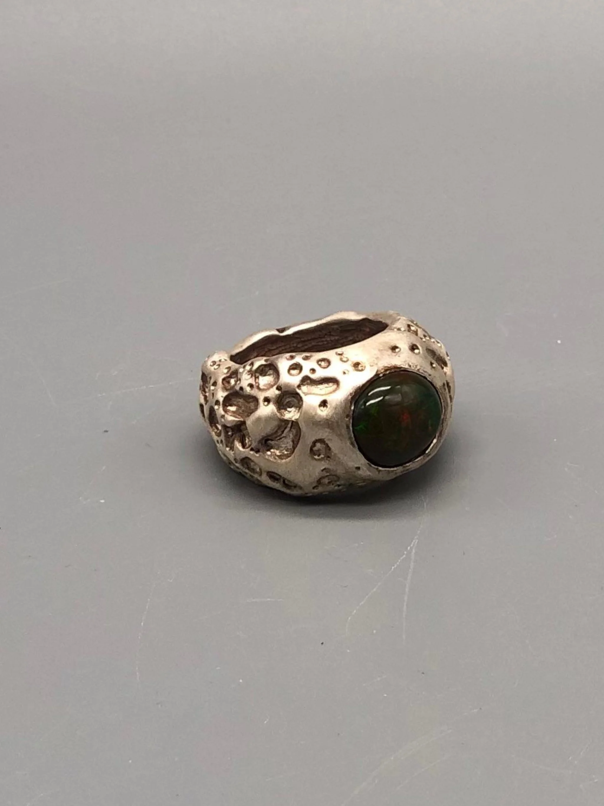 Luna ring by Portas Jewels in textured silver with a black opal showing deep red and green reflections.