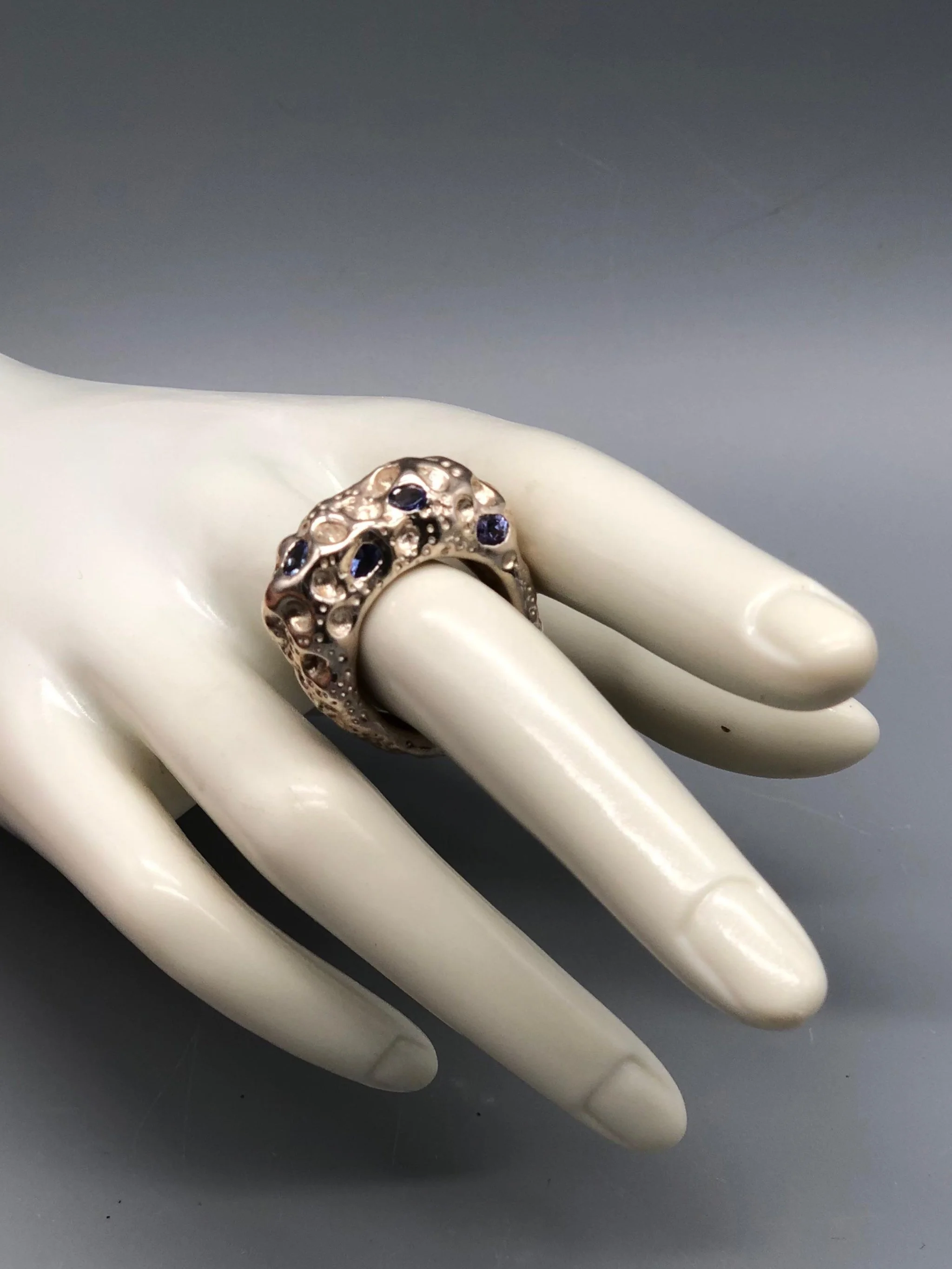 Anello Luna di Portas in argento con quattro tanzaniti blu incastonate su una superficie lavorata con incisioni, cavità e rilievi.