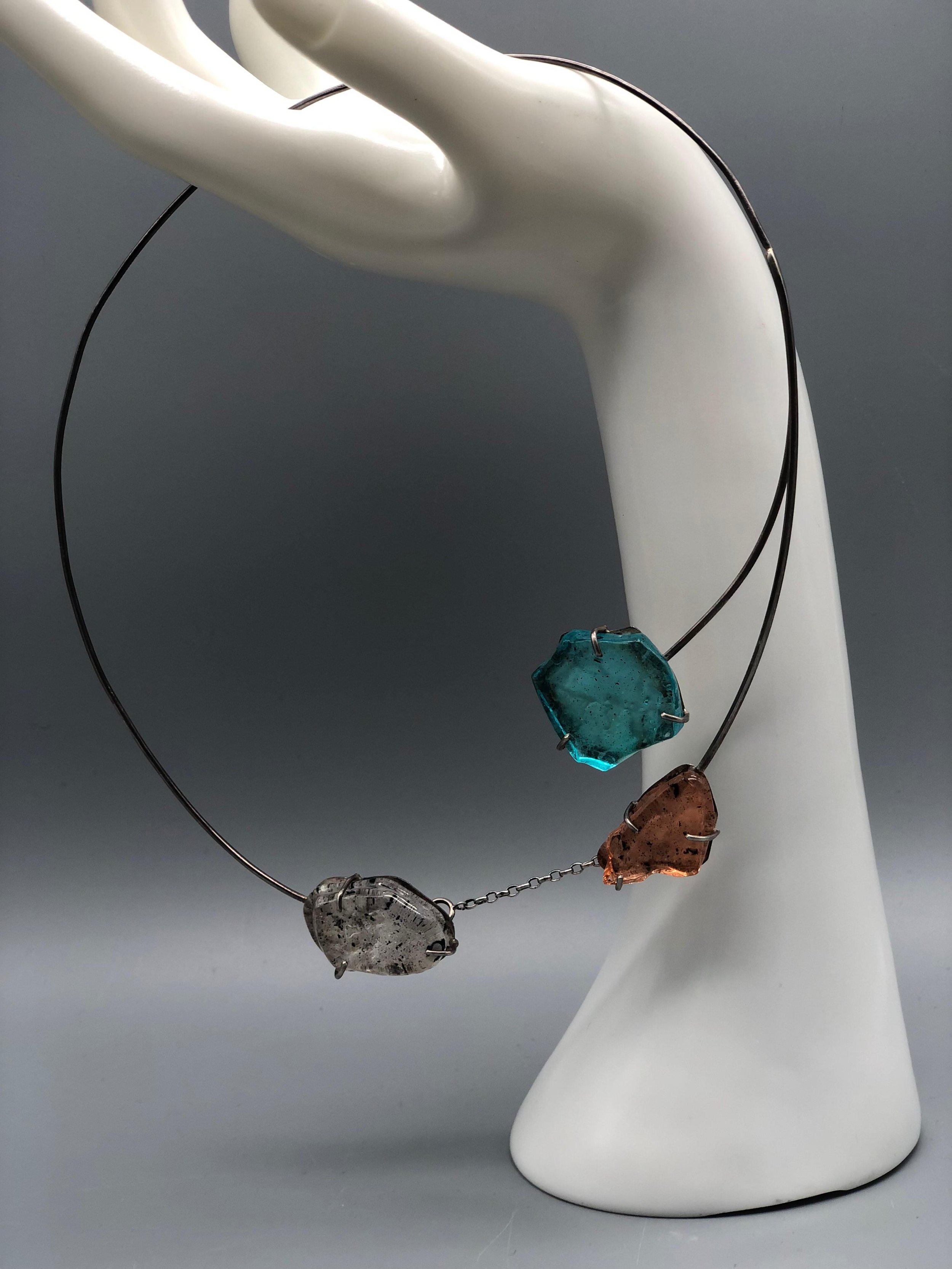 Manumara Arte Design — contemporary necklace with sculptural fused glass elements in blue, smoky grey and amber tones, available at Crepundia Gioielli Bologna.