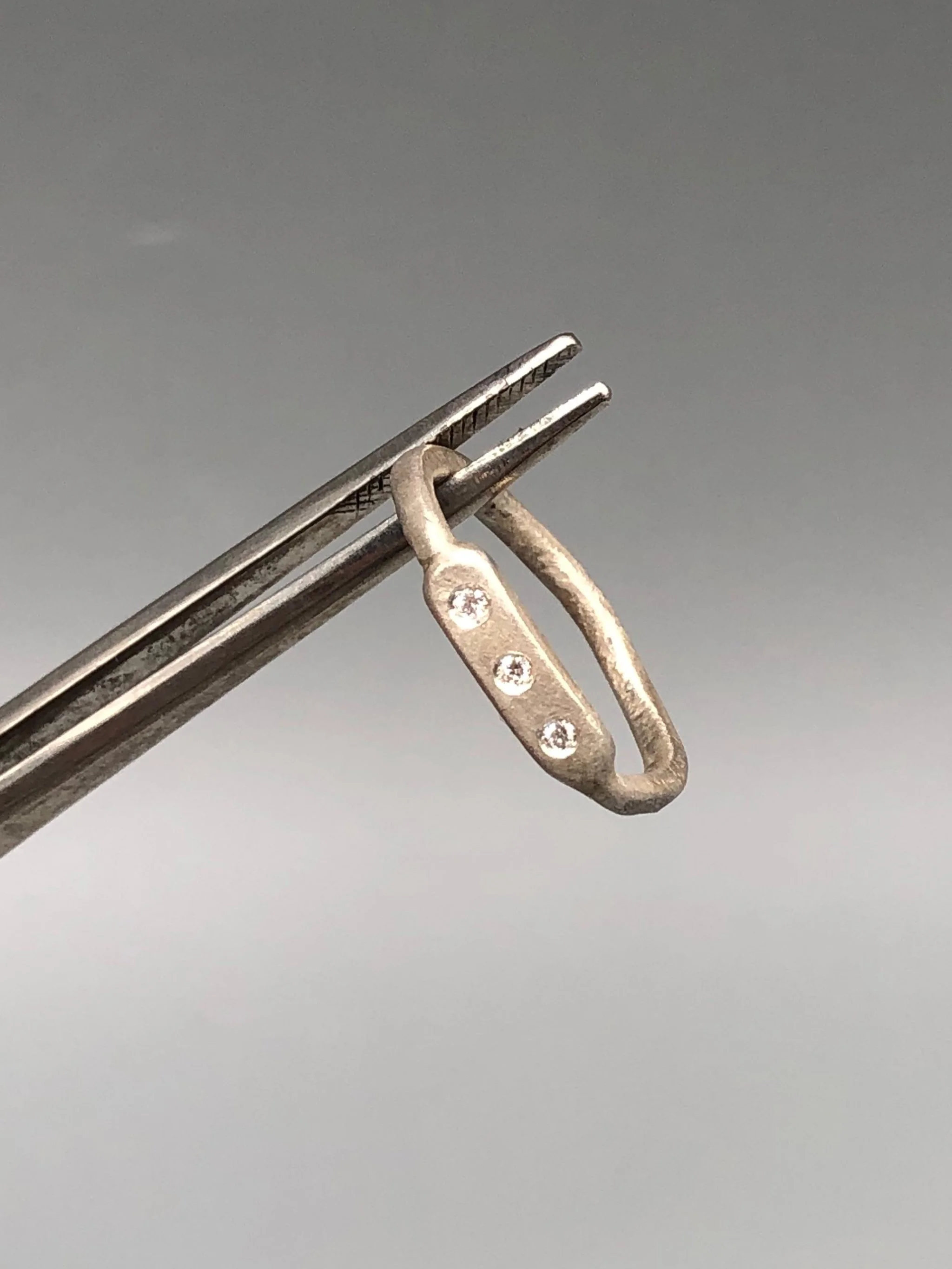 Anello Flat 3 di Crepundia Gioielli, argento dalla superficie irregolare con tre brillanti incastonati. Flat 3 ring by Crepundia Gioielli, silver with an irregular surface and three flush-set diamonds