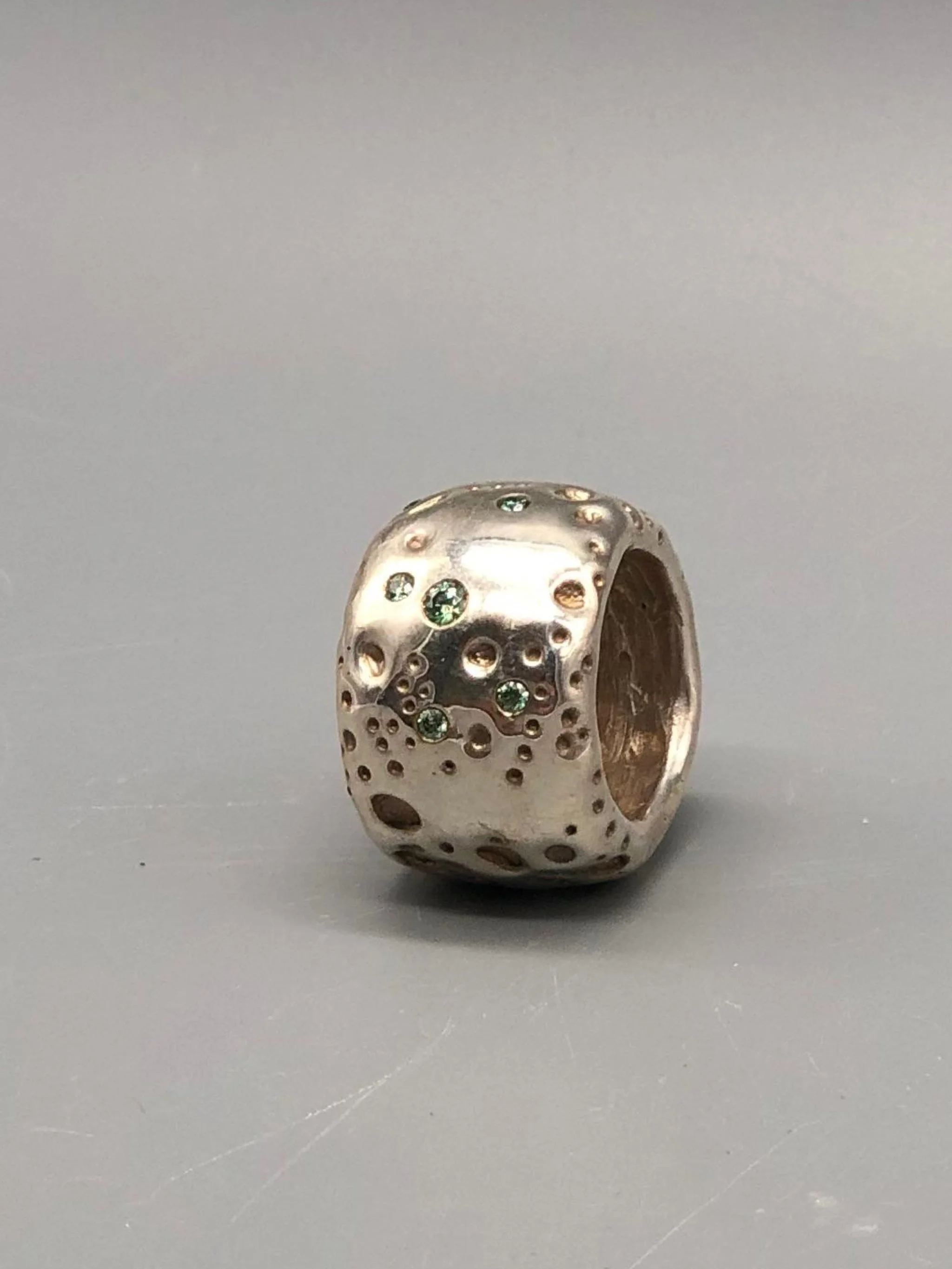 Portas Luna ring with green moissanites, featuring an irregular cratered surface inspired by a lunar landscape.