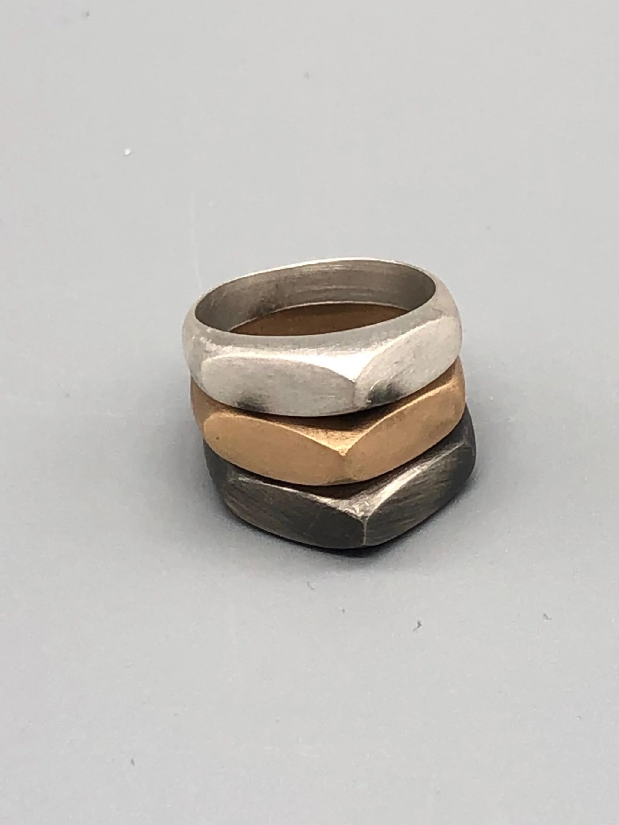 Tre anelli Cuspide di Crepundia Gioielli in argento, argento brunito e bronzo, sovrapposti in una composizione geometrica e scultorea.  Three Crepundia Cuspide rings in sterling silver, oxidized silve