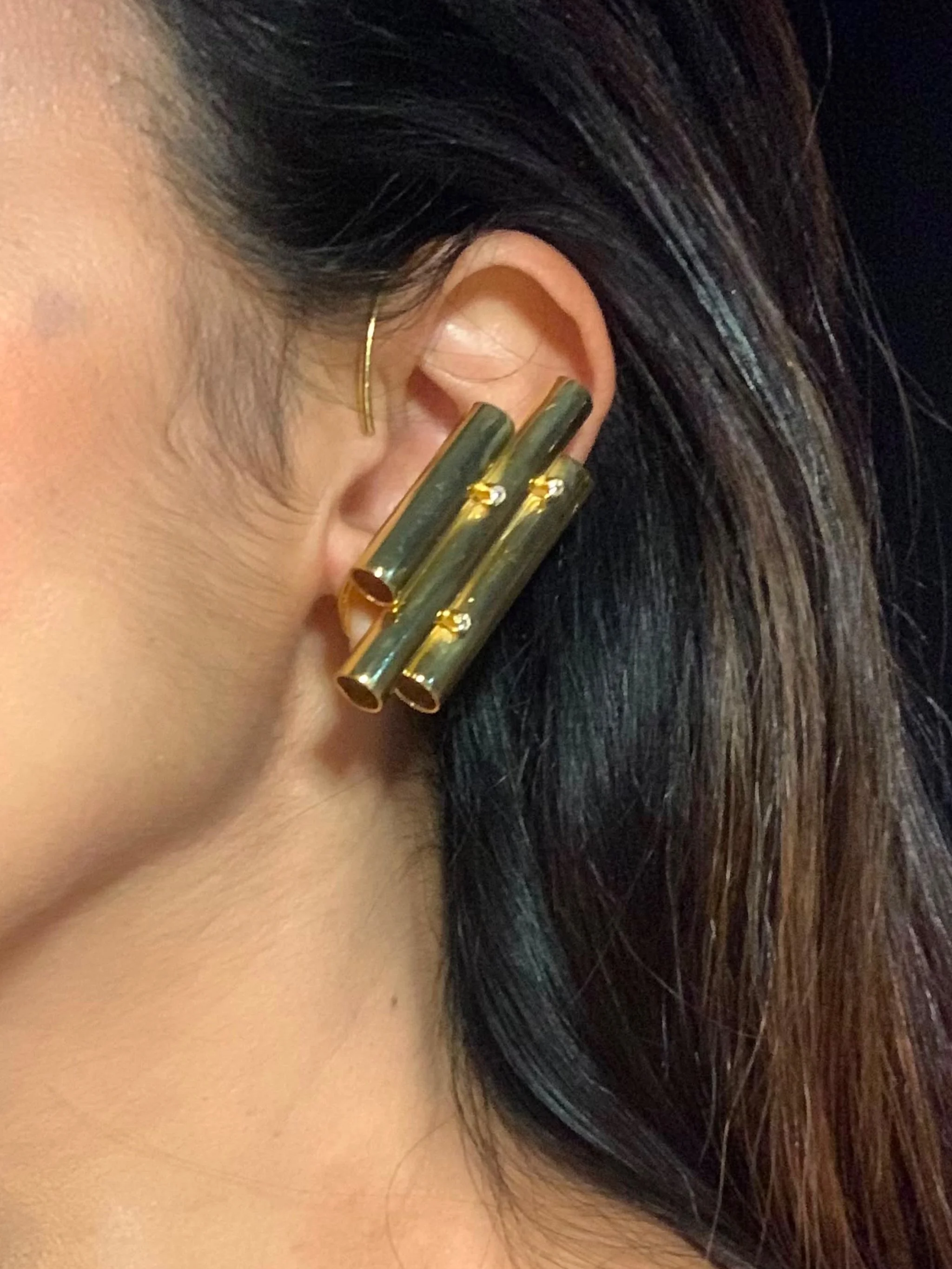 The Earcuff di HoAsen, ear cuff dorato con cilindri asimmetrici. The Earcuff by HoAsen, gold-tone ear cuff with asymmetrical cylinders.