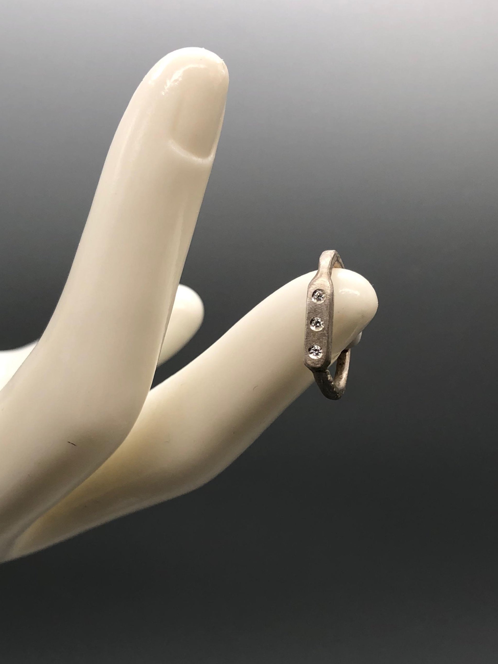 Anello Flat 3 di Crepundia Gioielli, argento dalla superficie irregolare con tre brillanti incastonati. Flat 3 ring by Crepundia Gioielli, silver with an irregular surface and three flush-set diamonds