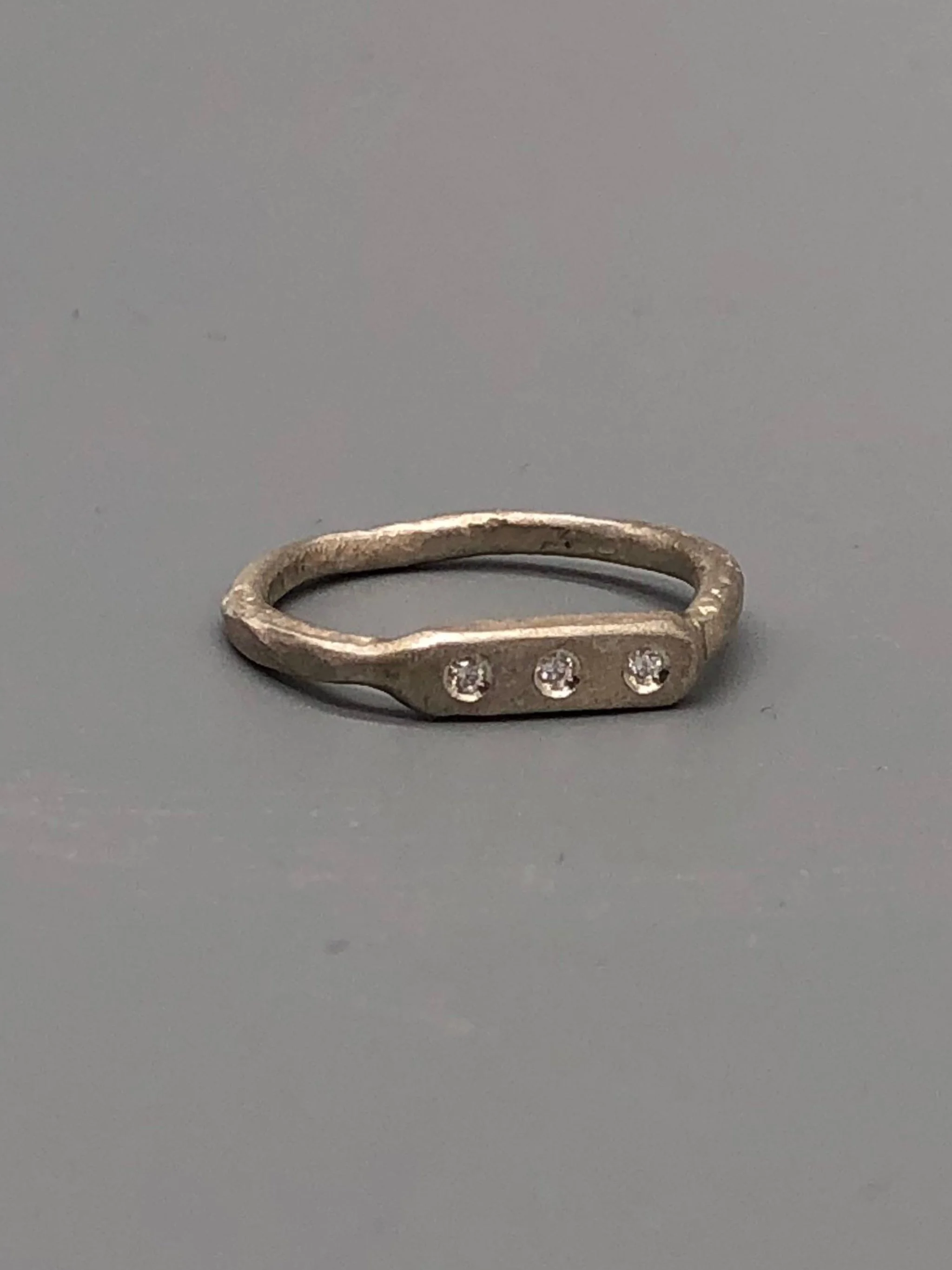 Anello Flat 3 di Crepundia Gioielli, argento dalla superficie irregolare con tre brillanti incastonati. Flat 3 ring by Crepundia Gioielli, silver with an irregular surface and three flush-set diamonds