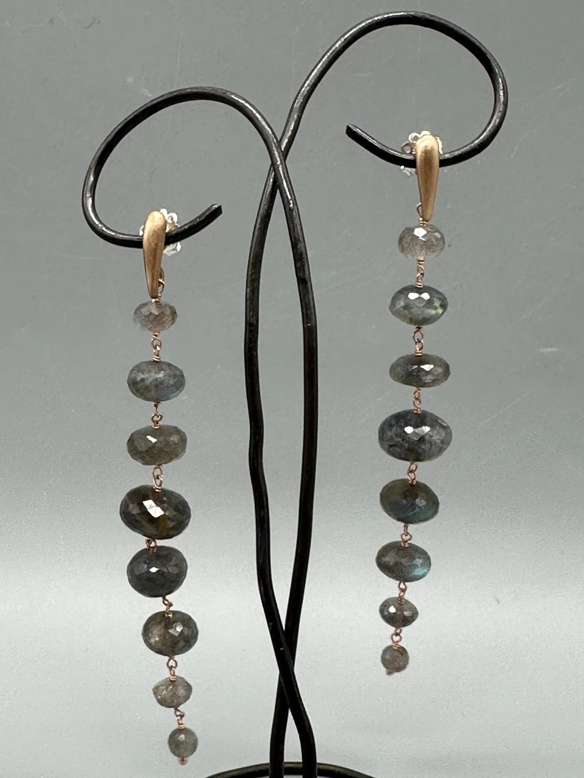 Orecchini Bold Labradorite con pietre grigie sfaccettate dai riflessi blu e verdi, disposte in verticale. Bold Labradorite earrings with vertically arranged faceted grey gemstones and blue-green refle
