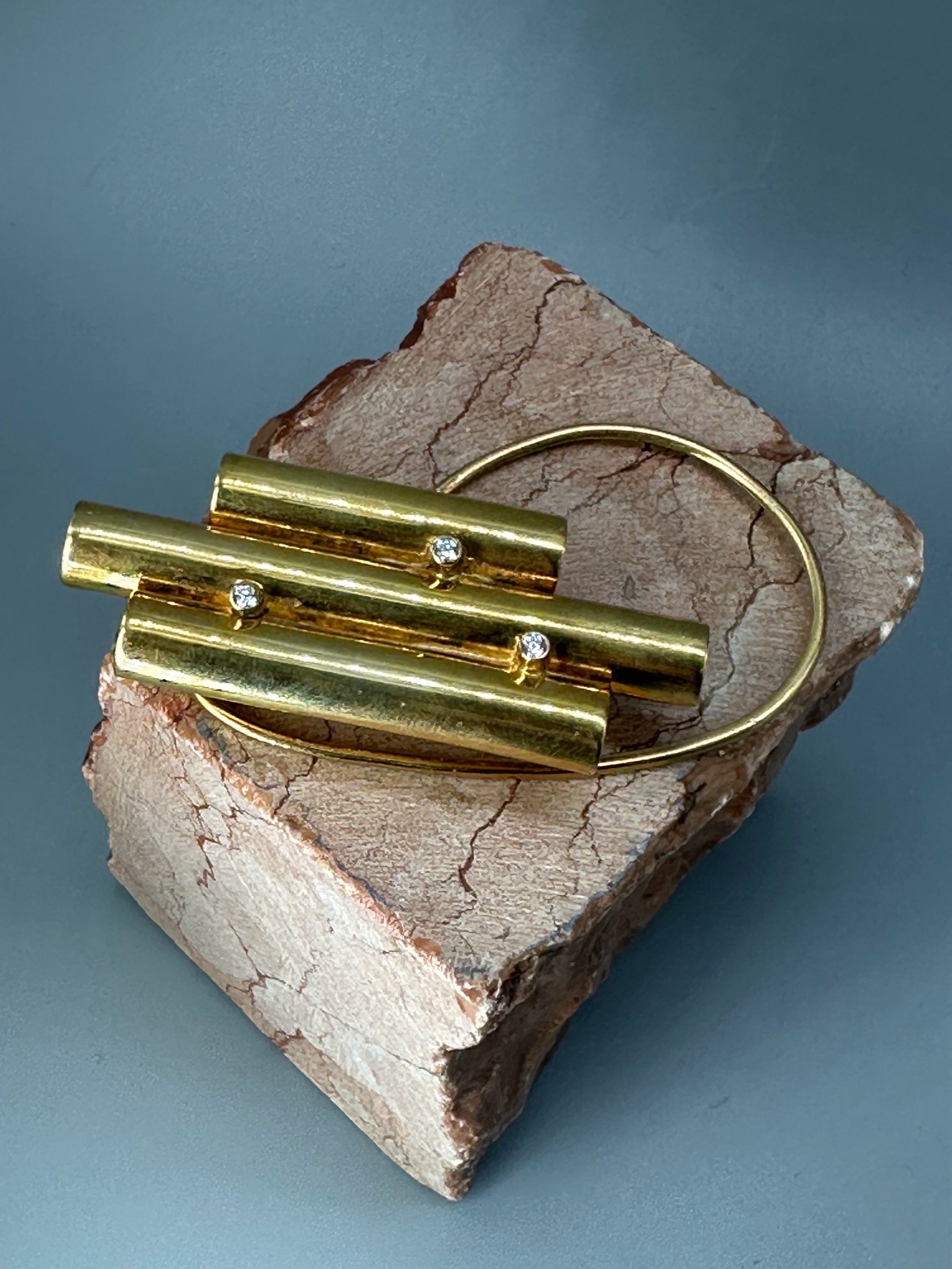 The Earcuff di HoAsen, ear cuff dorato con cilindri asimmetrici. The Earcuff by HoAsen, gold-tone ear cuff with asymmetrical cylinders.