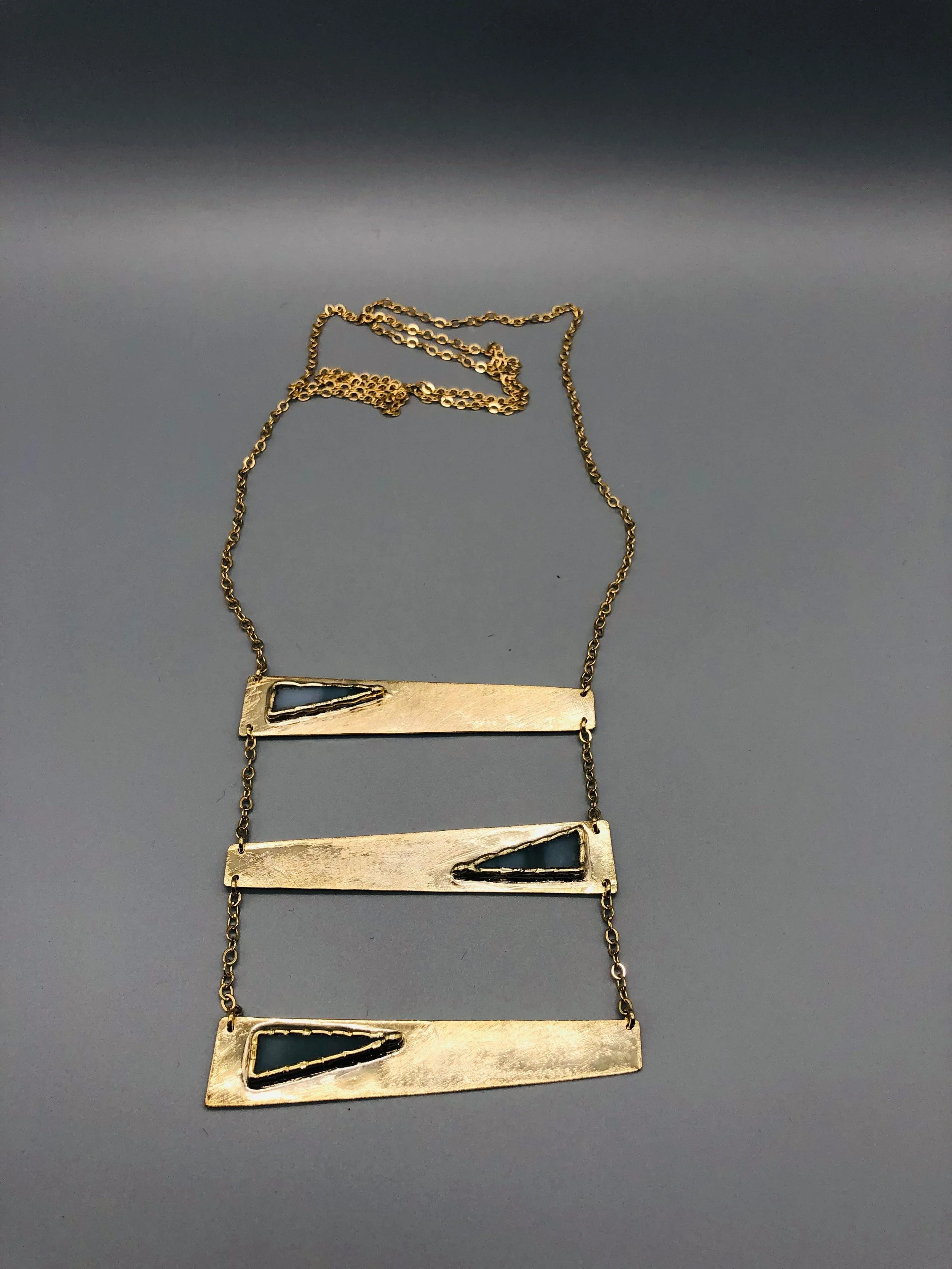 Collana Tris Grigia di Anni Luce in ottone dorato e vetro di Murano grigio, con tre elementi geometrici asimmetrici.
