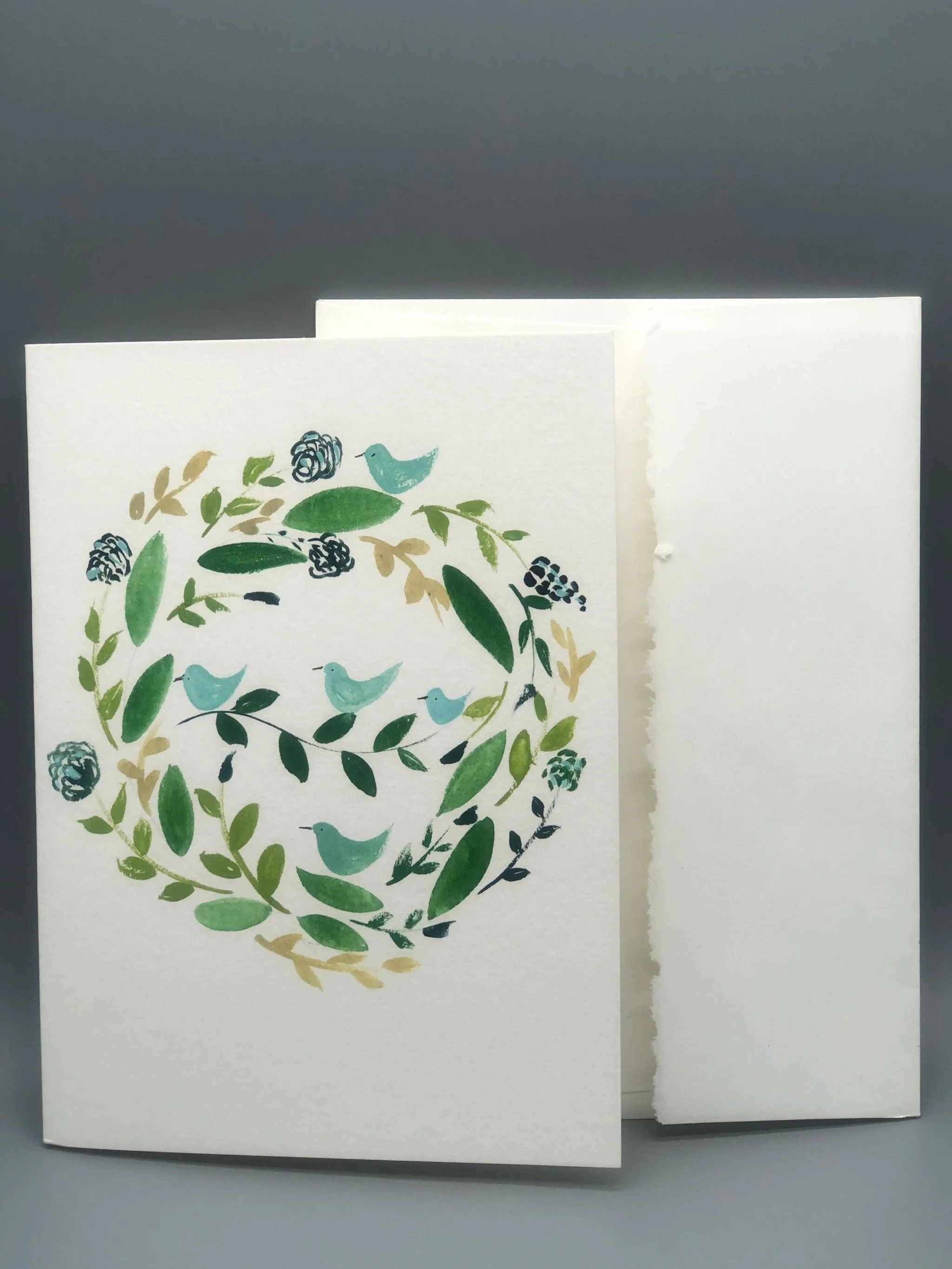 Botanical wreath watercolor card by Martina Catenacci for Crepundia Gioielli Bologna, hand-painted on fine art paper with pale green birds and matching envelope