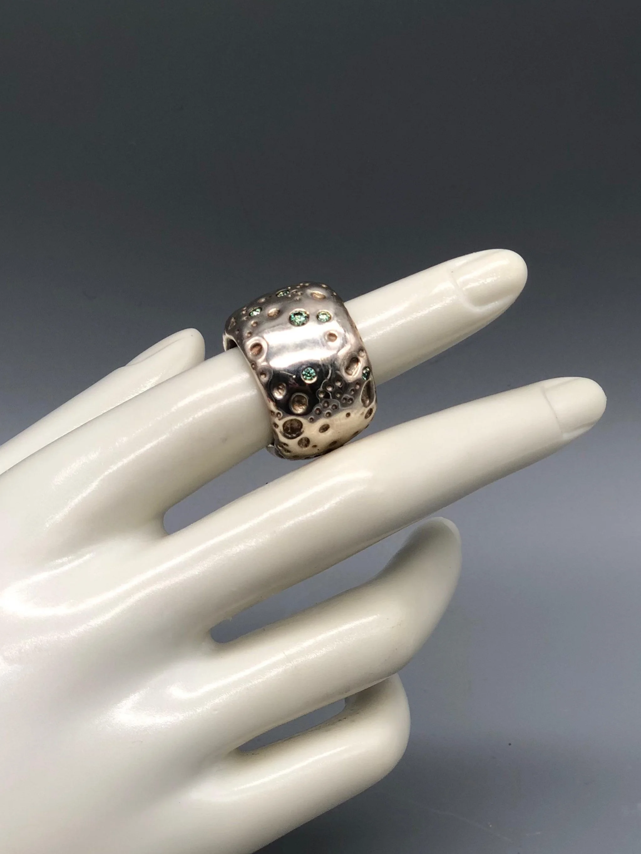 Portas Luna ring with green moissanites, featuring an irregular cratered surface inspired by a lunar landscape.