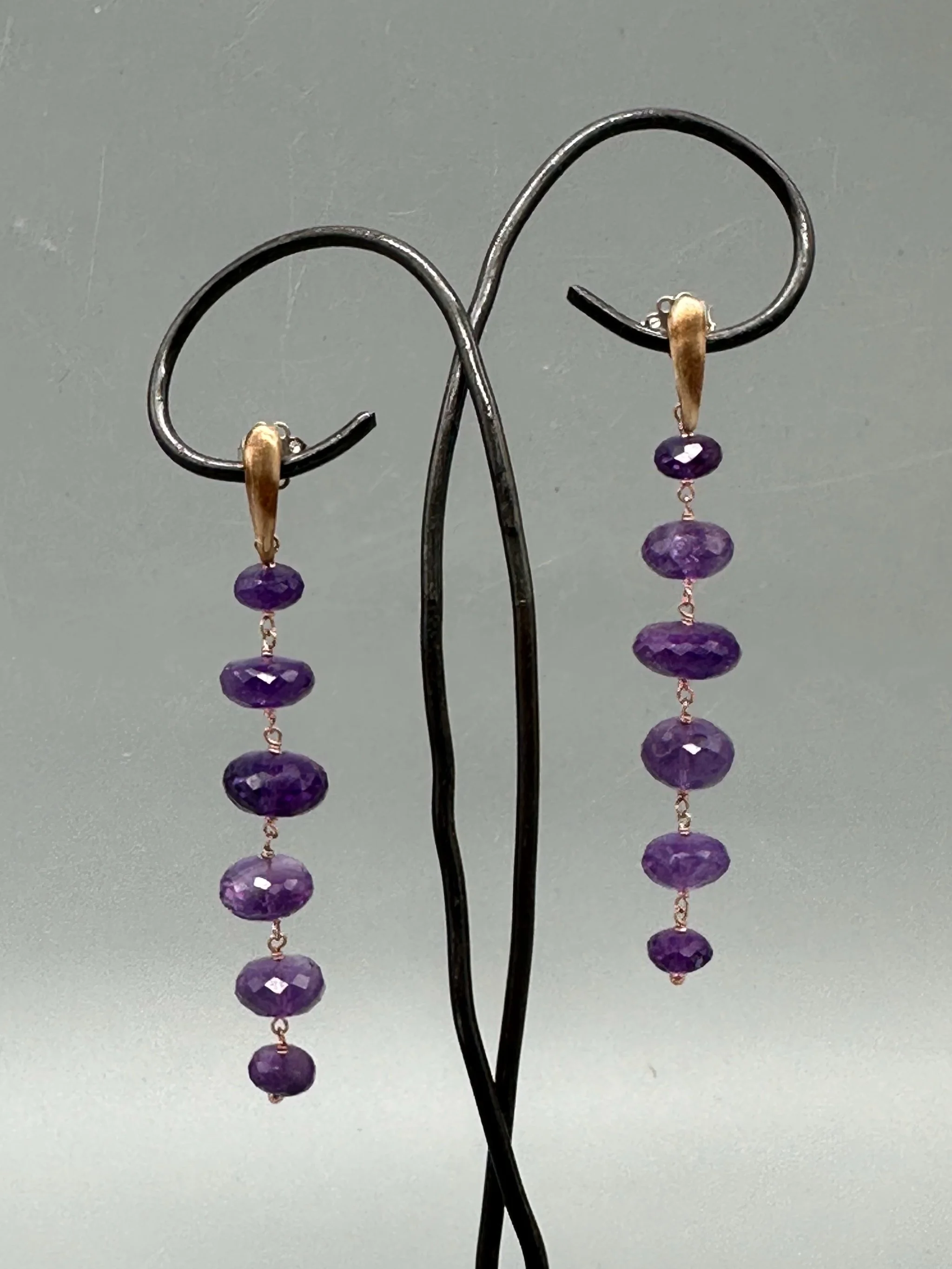 Orecchini Bold Ametista con pietre viola sfaccettate e montatura essenziale. Bold Amethyst earrings with faceted purple gemstones and a minimal metal setting.