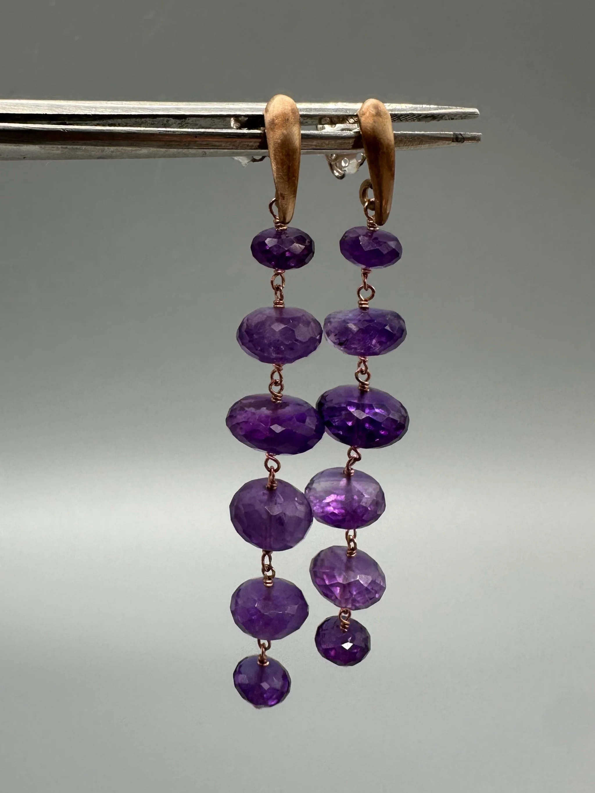 Orecchini Bold Ametista con pietre viola sfaccettate e montatura essenziale. Bold Amethyst earrings with faceted purple gemstones and a minimal metal setting.