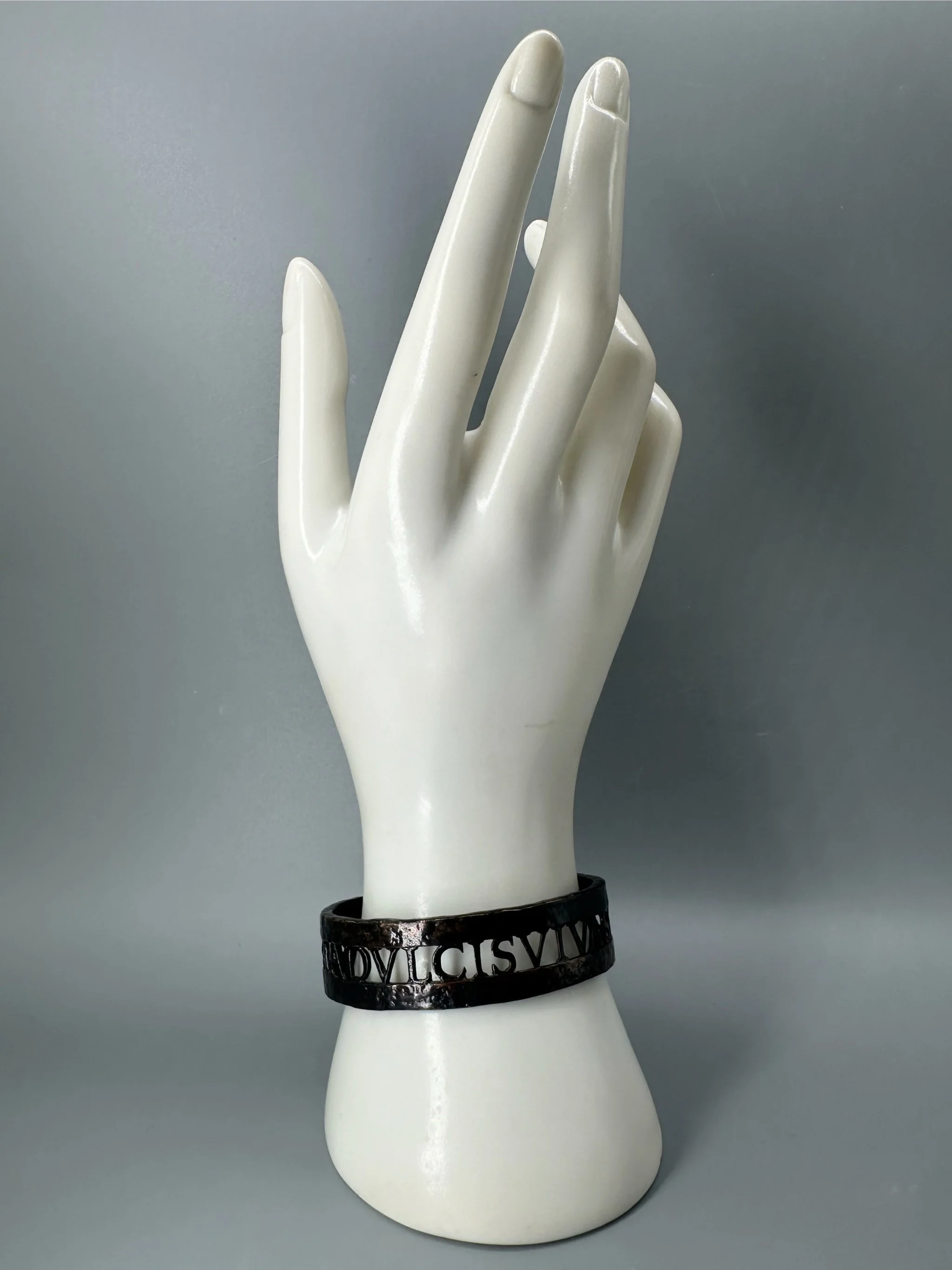Bracciale Anima Dulcis di CōDICEDS in bronzo brunito, aperto e regolabile, con iscrizione latina traforata.  CōDICEDS Anima Dulcis open adjustable cuff in darkened bronze with openwork Latin inscripti