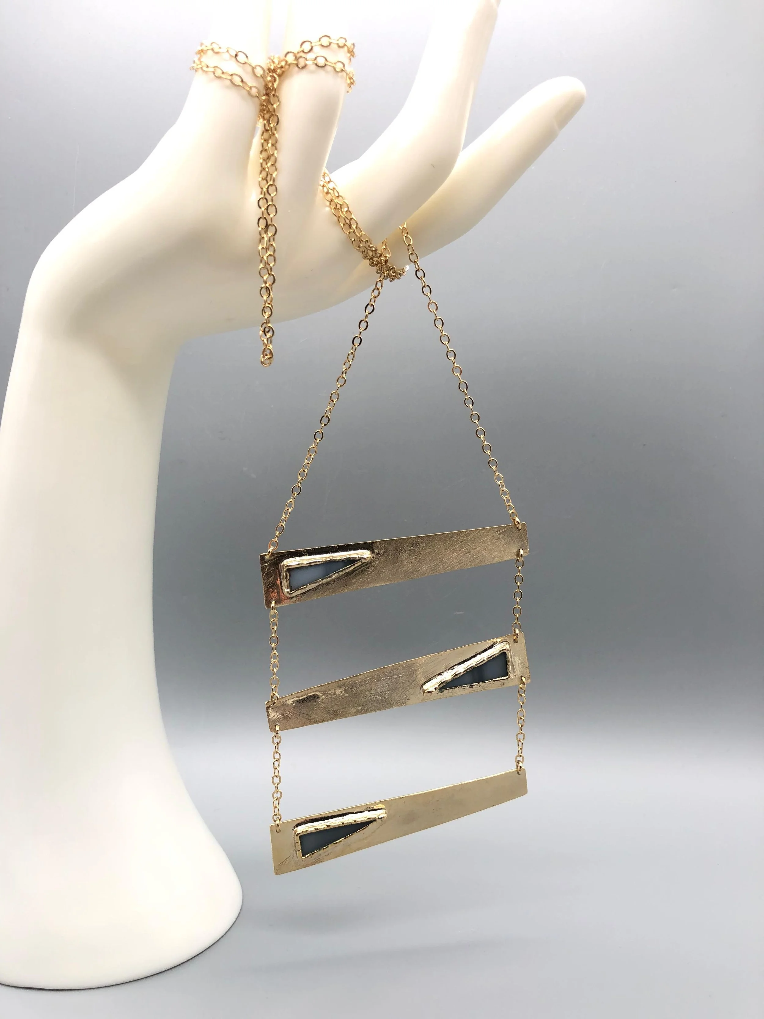 Collana Tris Grigia di Anni Luce in ottone dorato e vetro di Murano grigio, con tre elementi geometrici asimmetrici.