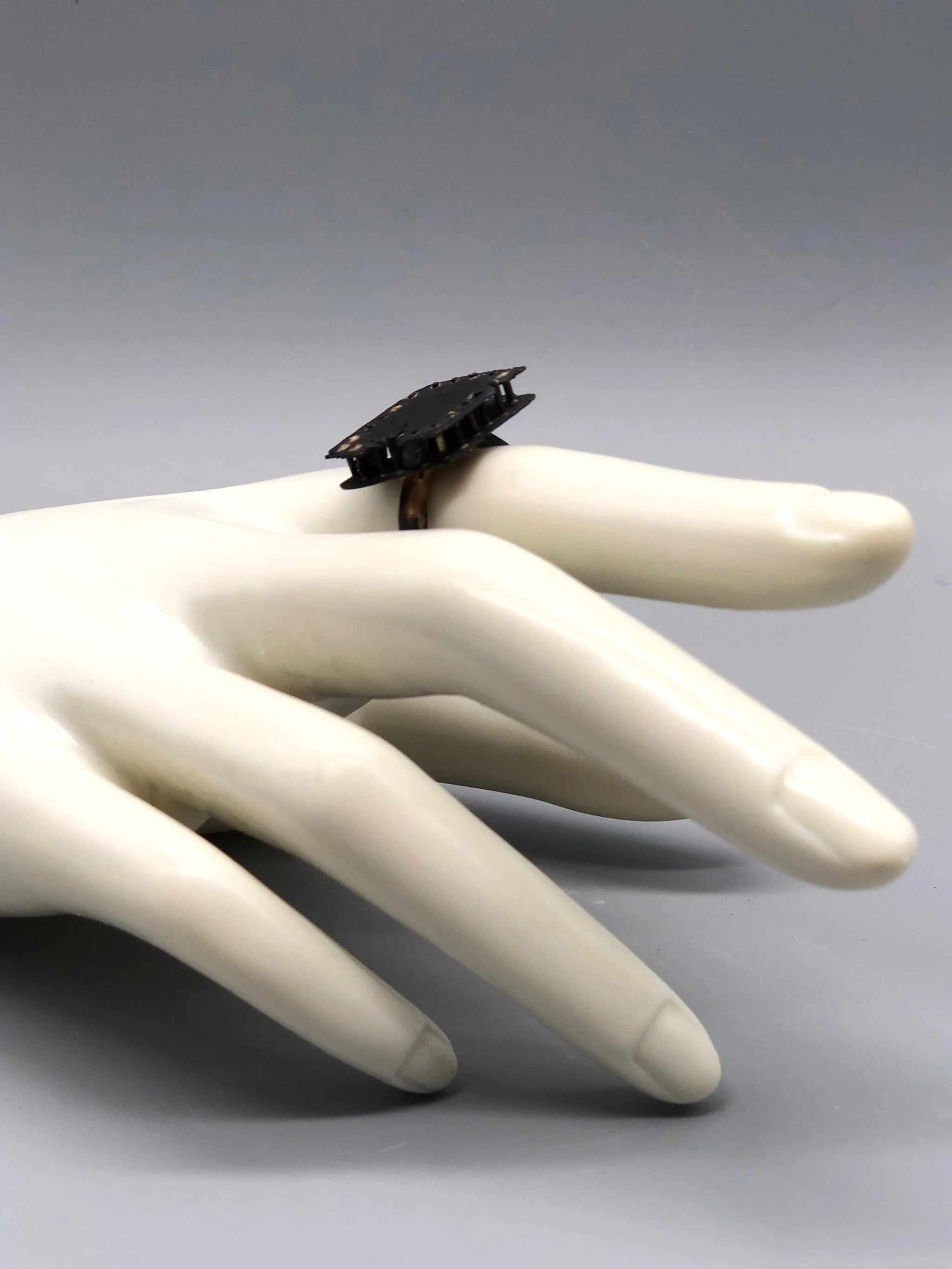 Anello Gabbia di Marco Mangàni in oro 14 kt e oro 18 kt ossidato, con struttura a sbarre e due diamanti grigi nascosti all’interno.
