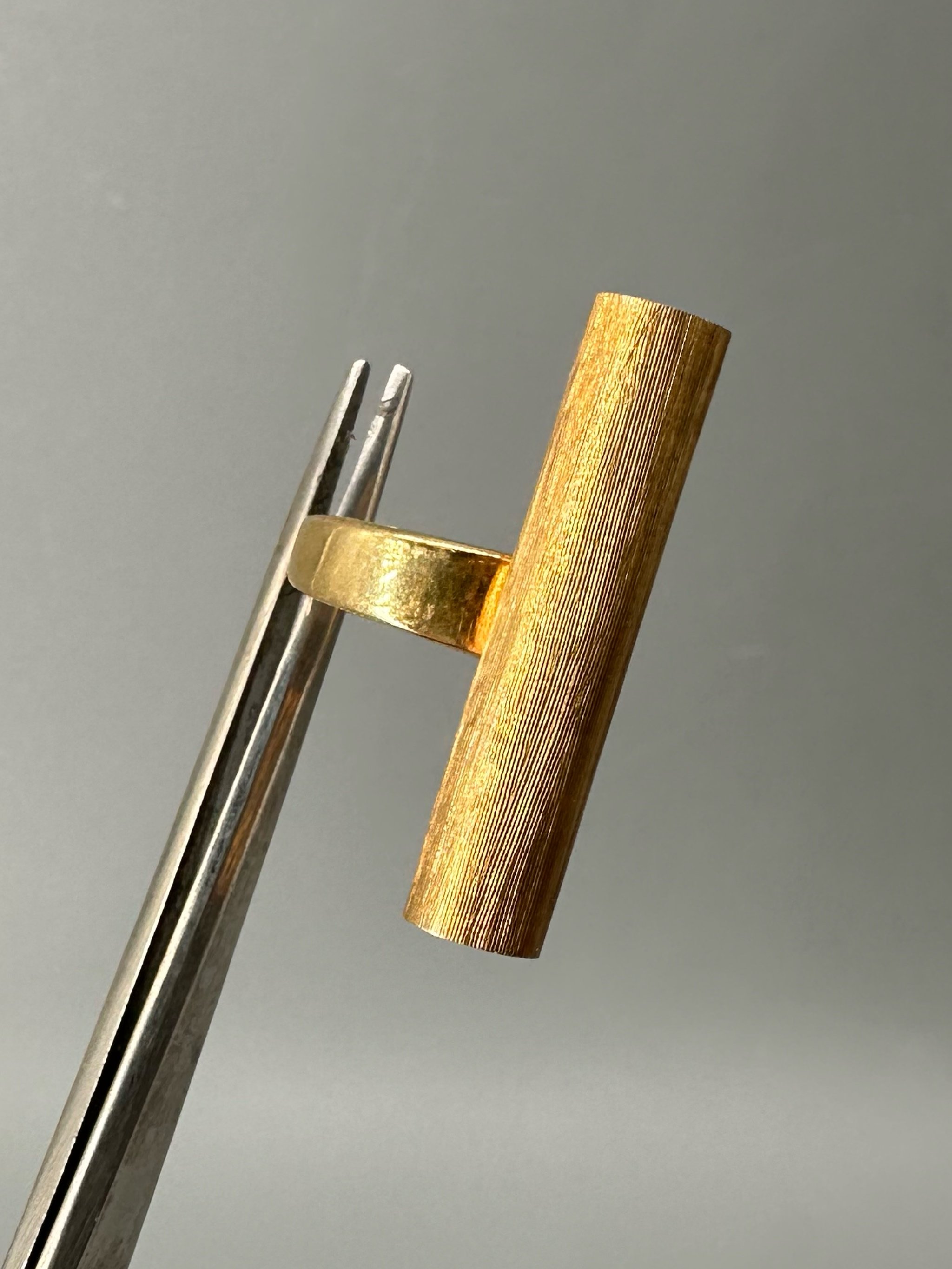 Anello Rough Tube di HoAsen Jewelry in argento dorato satinato, con elemento tubolare inciso.  Rough Tube ring by HoAsen Jewelry in satin-finished gold-plated silver, with a textured tubular element.