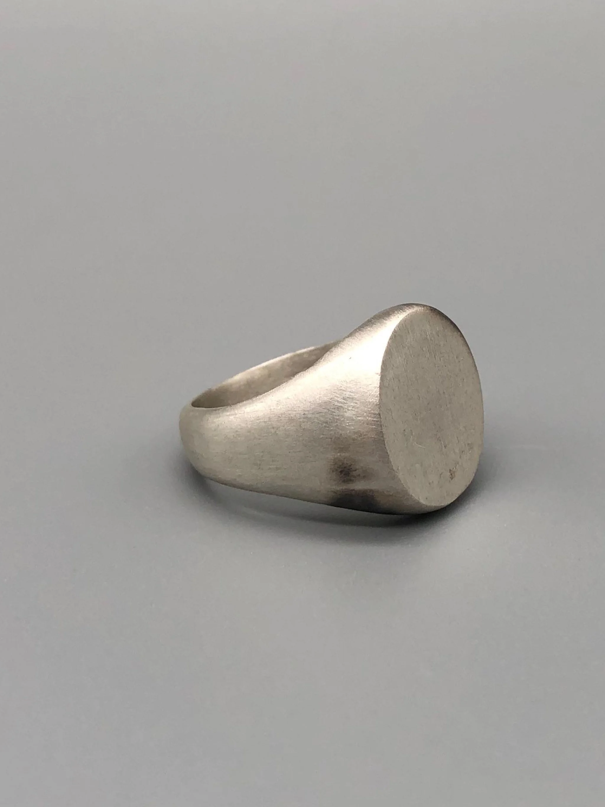 Anello Chevalière in argento opaco, gioiello contemporaneo dal volume pieno e dal design essenziale. Chevalière ring in matte silver, contemporary jewellery with a solid volume and essential design.