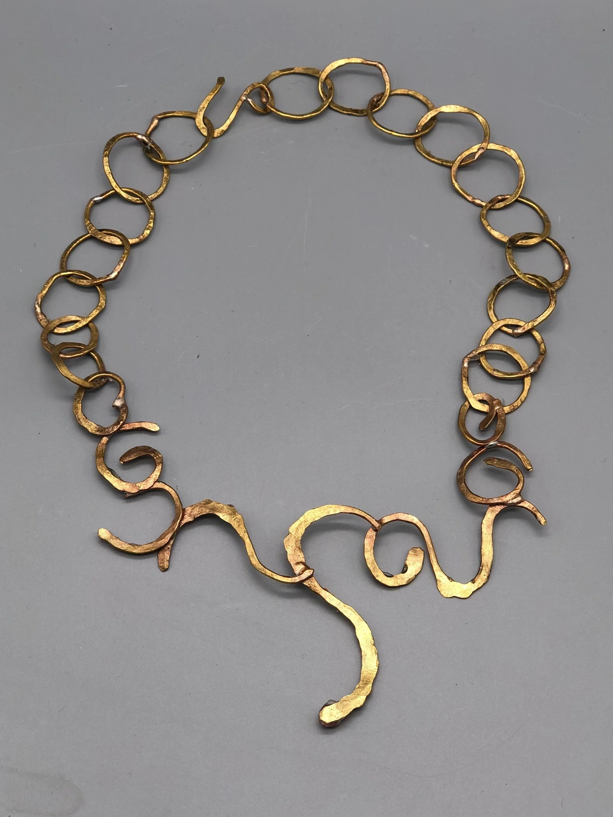 Collana Free Line di Claudia Cuzzeri in ottone opaco, con anelli irregolari e elemento centrale scultoreo a linea libera.