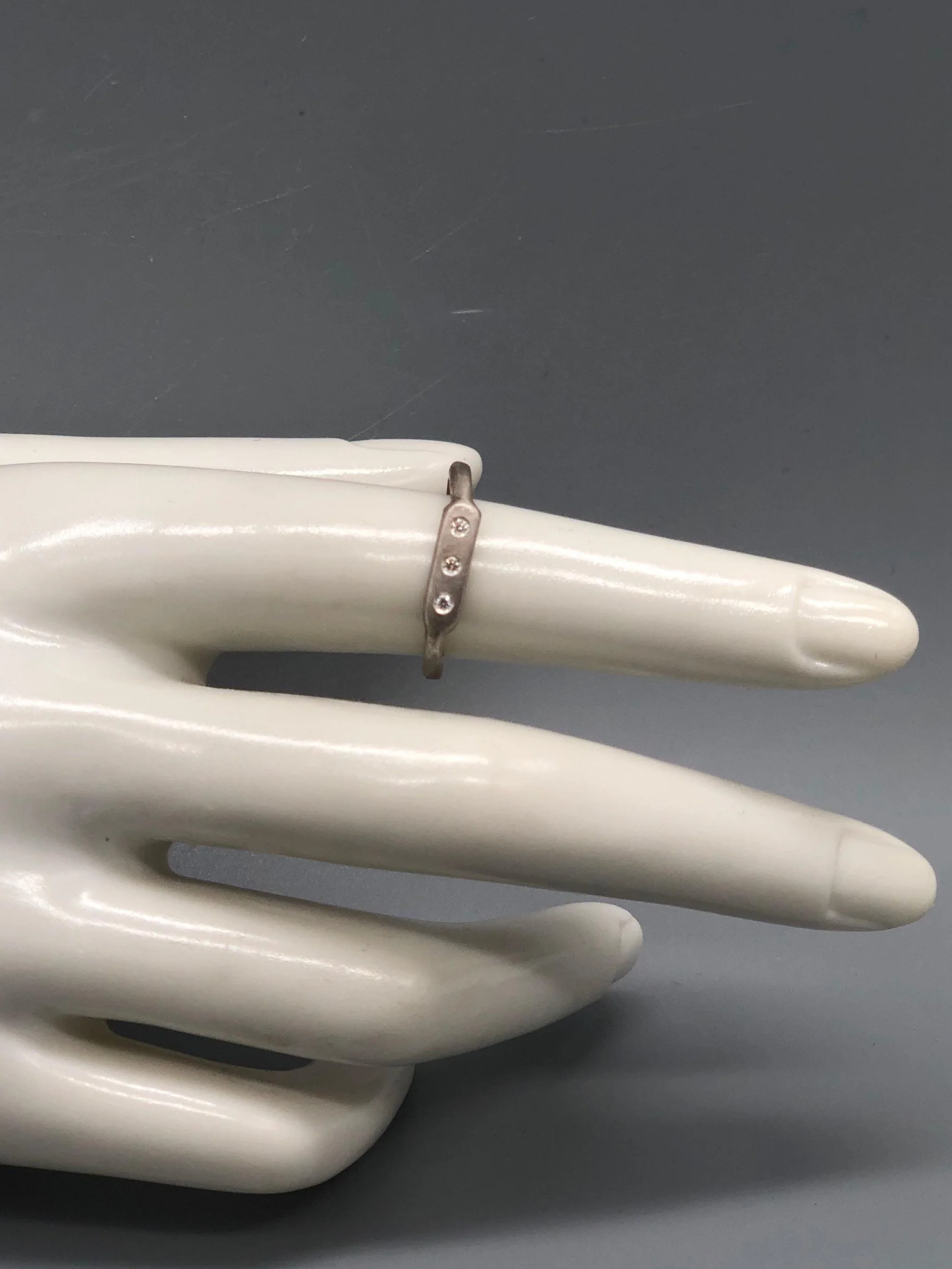 Anello Flat 3 di Crepundia Gioielli, argento dalla superficie irregolare con tre brillanti incastonati. Flat 3 ring by Crepundia Gioielli, silver with an irregular surface and three flush-set diamonds