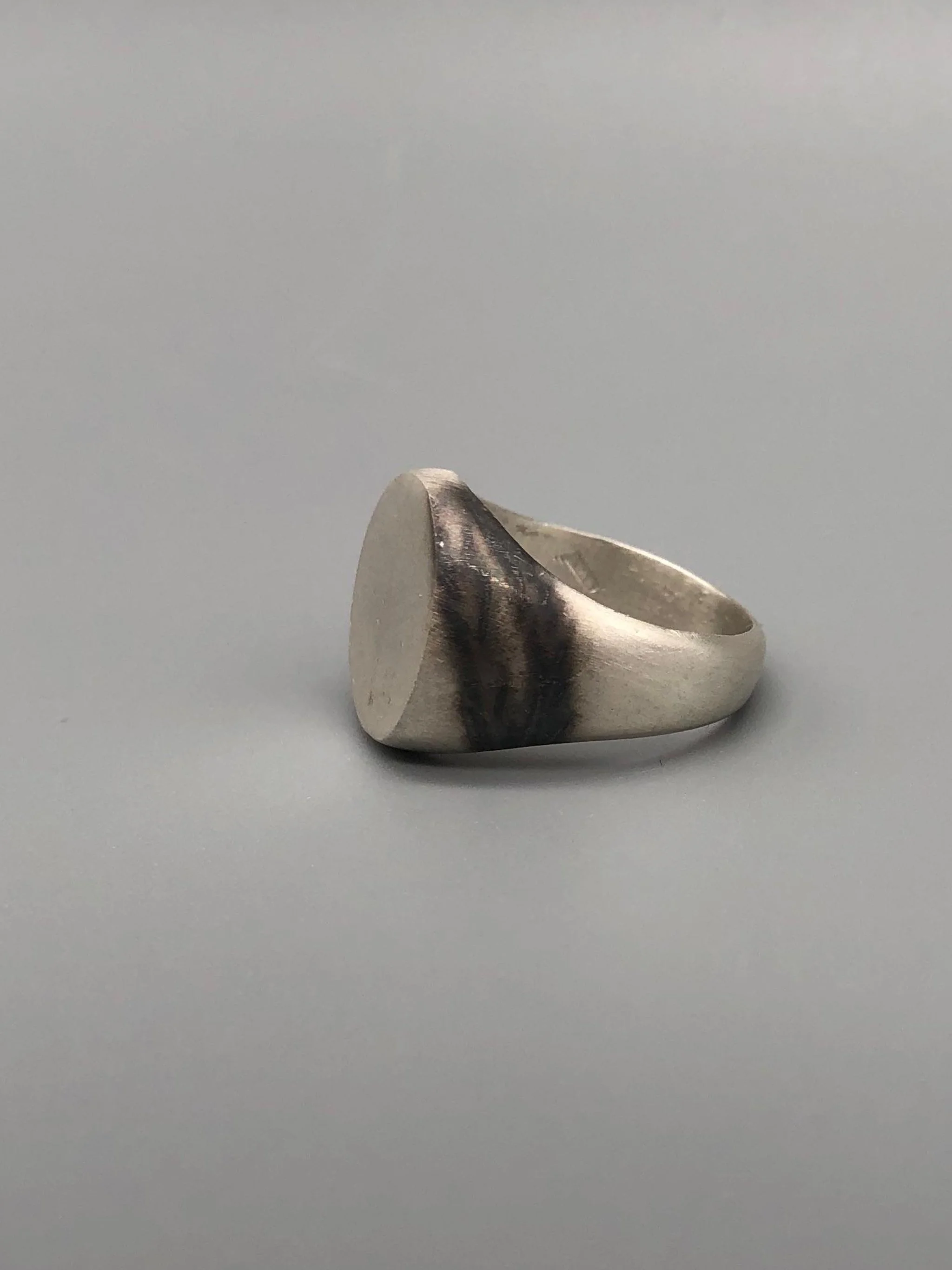 Anello Chevalière in argento opaco, gioiello contemporaneo dal volume pieno e dal design essenziale. Chevalière ring in matte silver, contemporary jewellery with a solid volume and essential design.