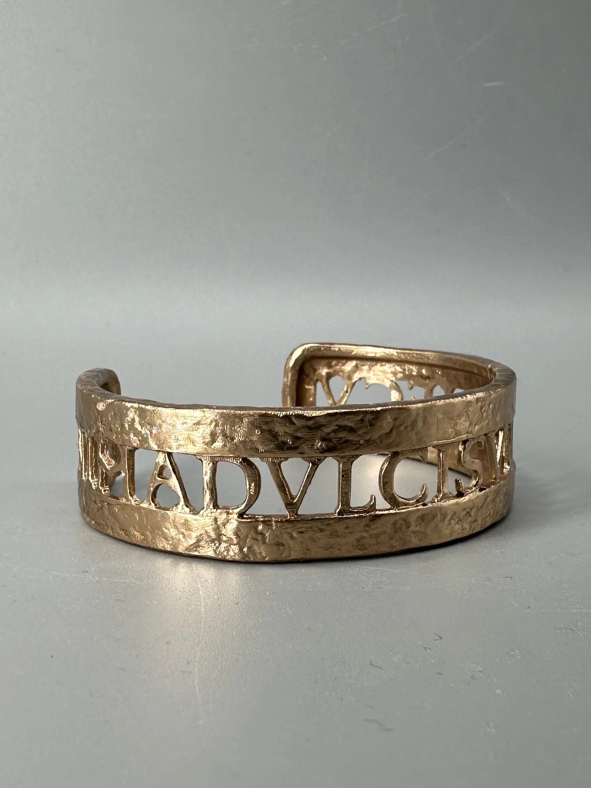 Bracciale Anima Dulcis di CōDICEDS in bronzo bocciardato, aperto e regolabile, con iscrizione latina traforata.  CōDICEDS Anima Dulcis open adjustable cuff in hammered bronze with openwork Latin inscr