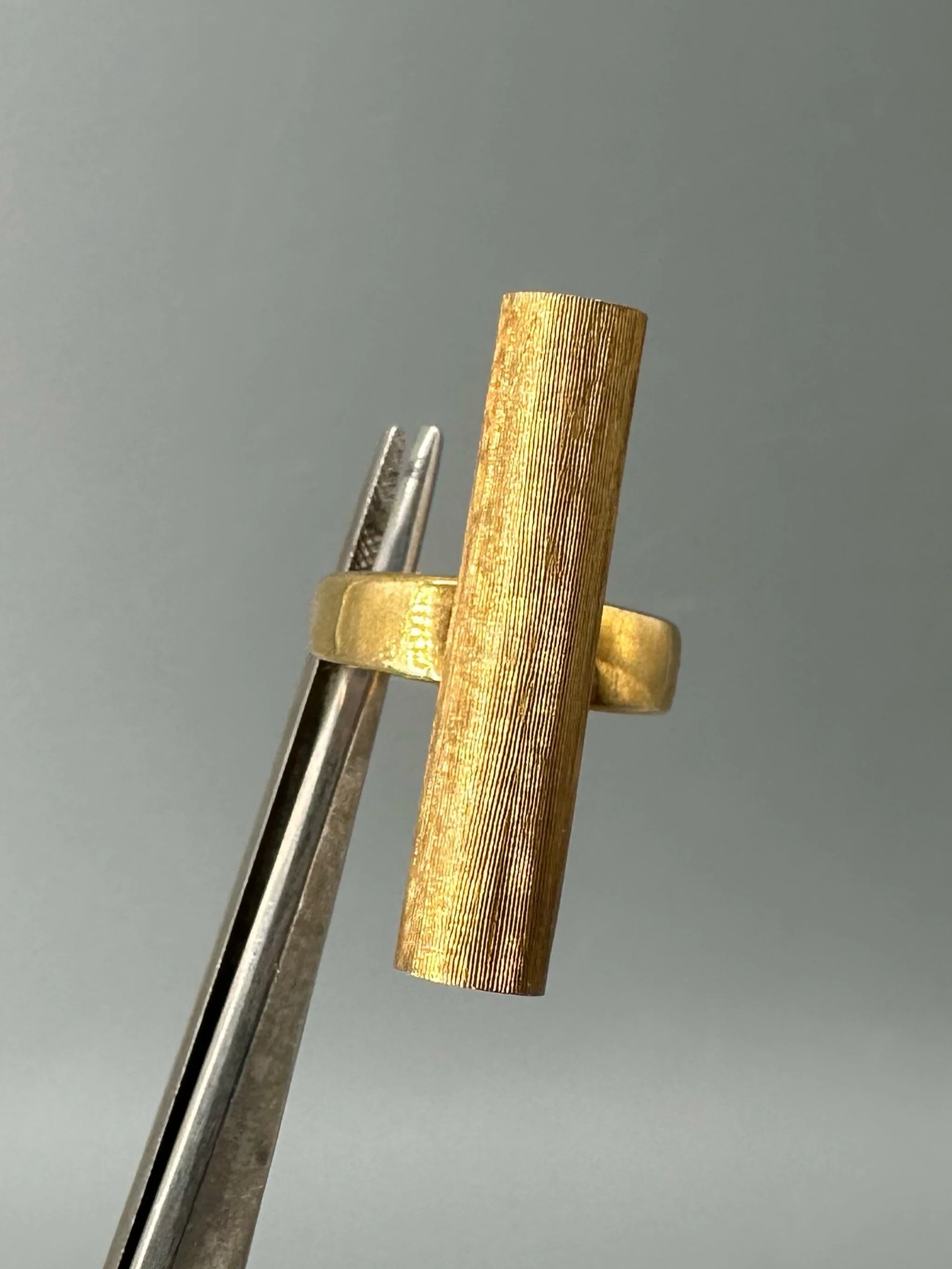 Anello Rough Tube di HoAsen Jewelry in argento dorato satinato, con elemento tubolare inciso.  Rough Tube ring by HoAsen Jewelry in satin-finished gold-plated silver, with a textured tubular element.