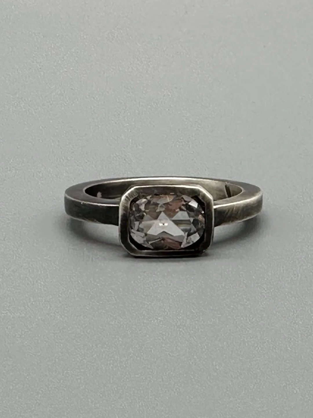 Anello White in Black in argento brunito con topazio bianco sfaccettato e castone geometrico. White in Black ring in oxidized sterling silver with faceted white topaz and geometric setting.