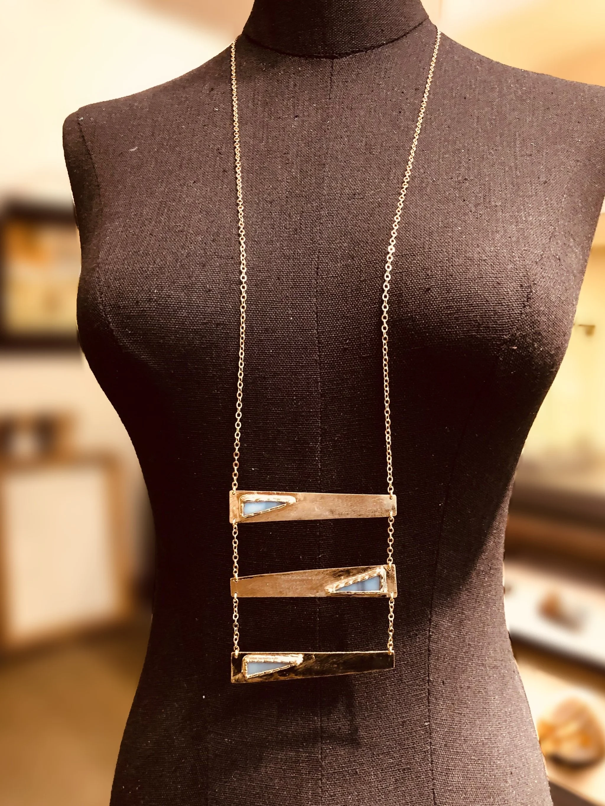 Collana Tris Grigia di Anni Luce in ottone dorato e vetro di Murano grigio, con tre elementi geometrici asimmetrici.