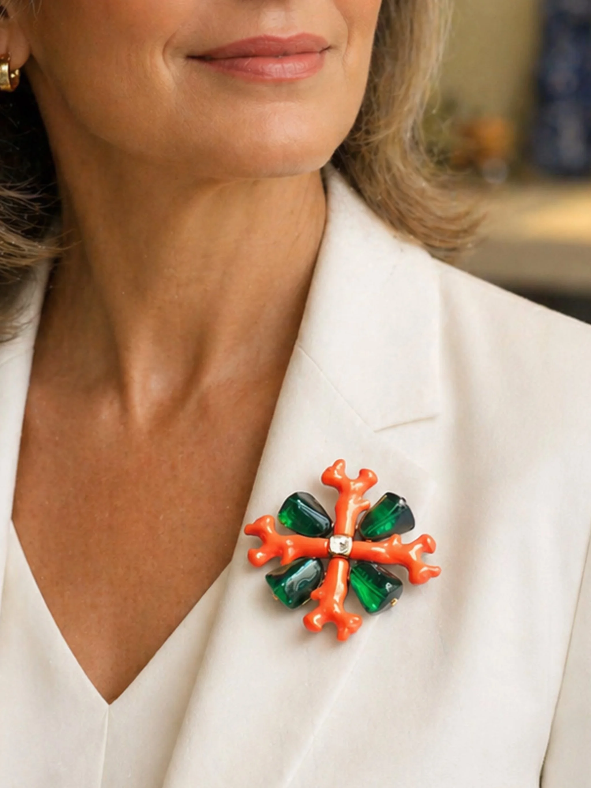 Kenneth Jay Lane coral-inspired brooch with orange branches and green cabochons, gold-tone, worn on white blazer — Crepundia Gioielli Bologna