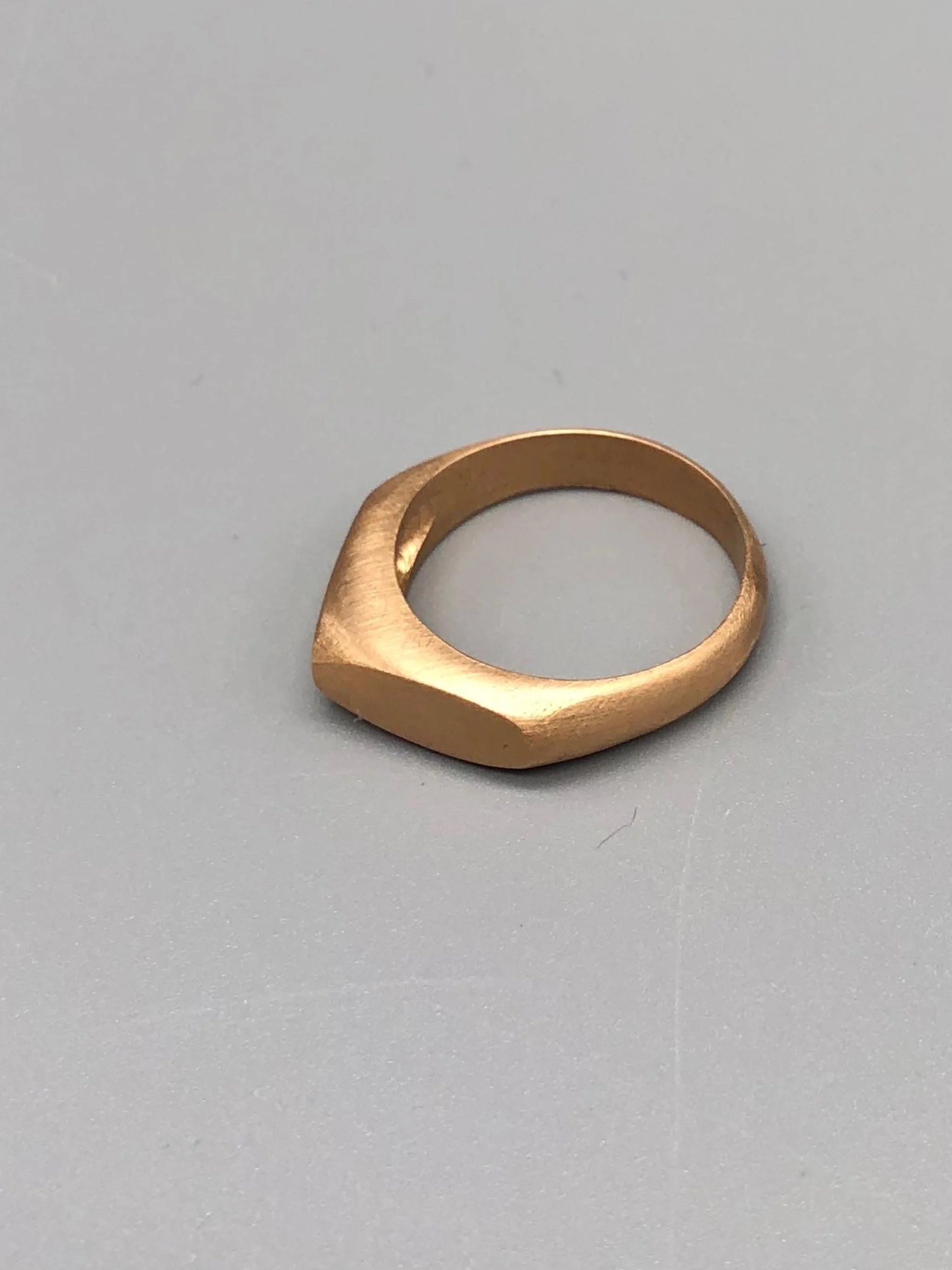 Anello Cuspide Crepundia in bronzo, con fascia geometrica, superfici sfaccettate e finitura satinata color oro caldo.  Crepundia Cuspide bronze ring featuring a geometric band, faceted surfaces and a
