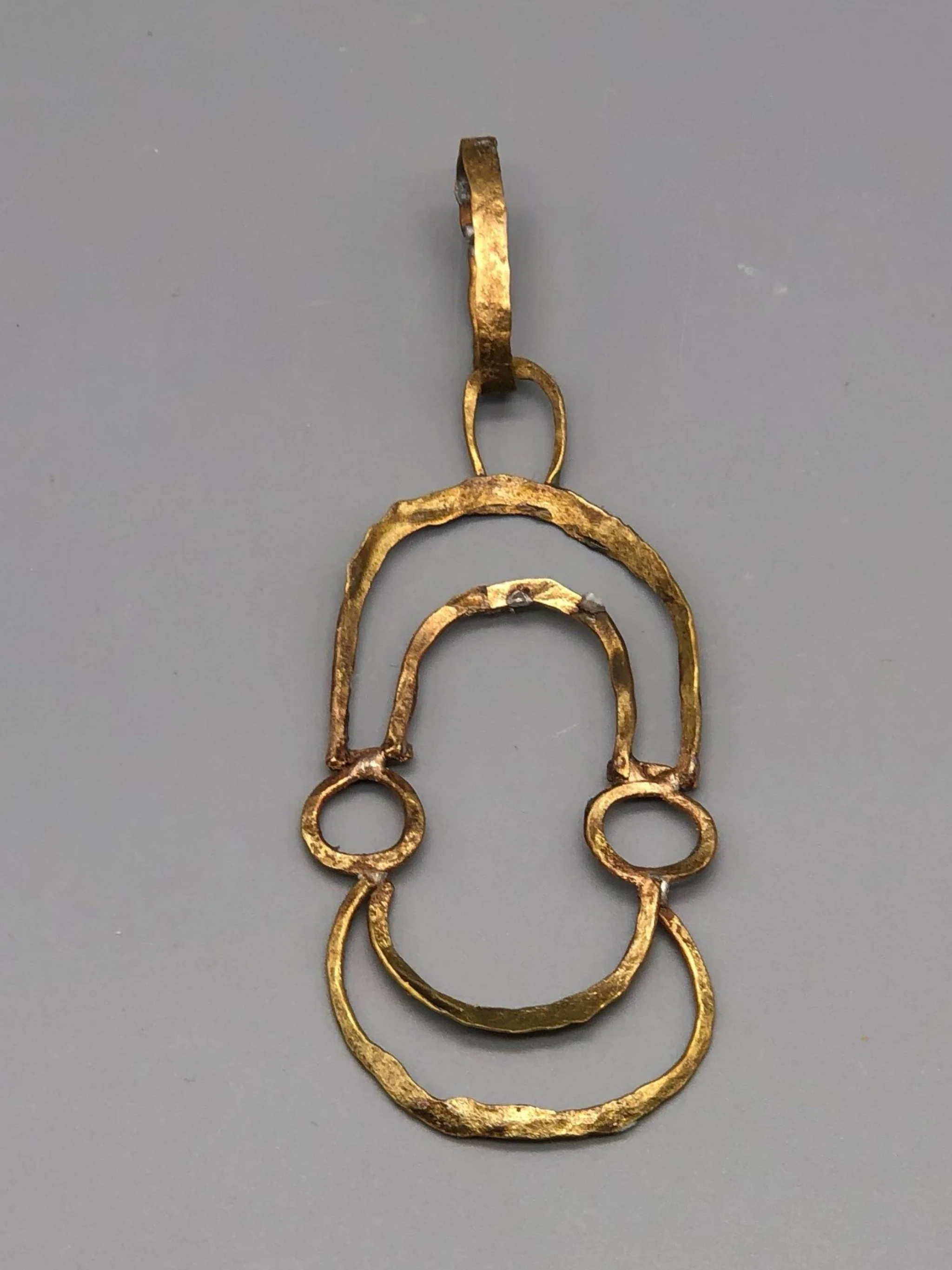 Ciondolo Contour di Claudia Cuzzeri in ottone opaco, con profili irregolari concentrici e forma aperta.