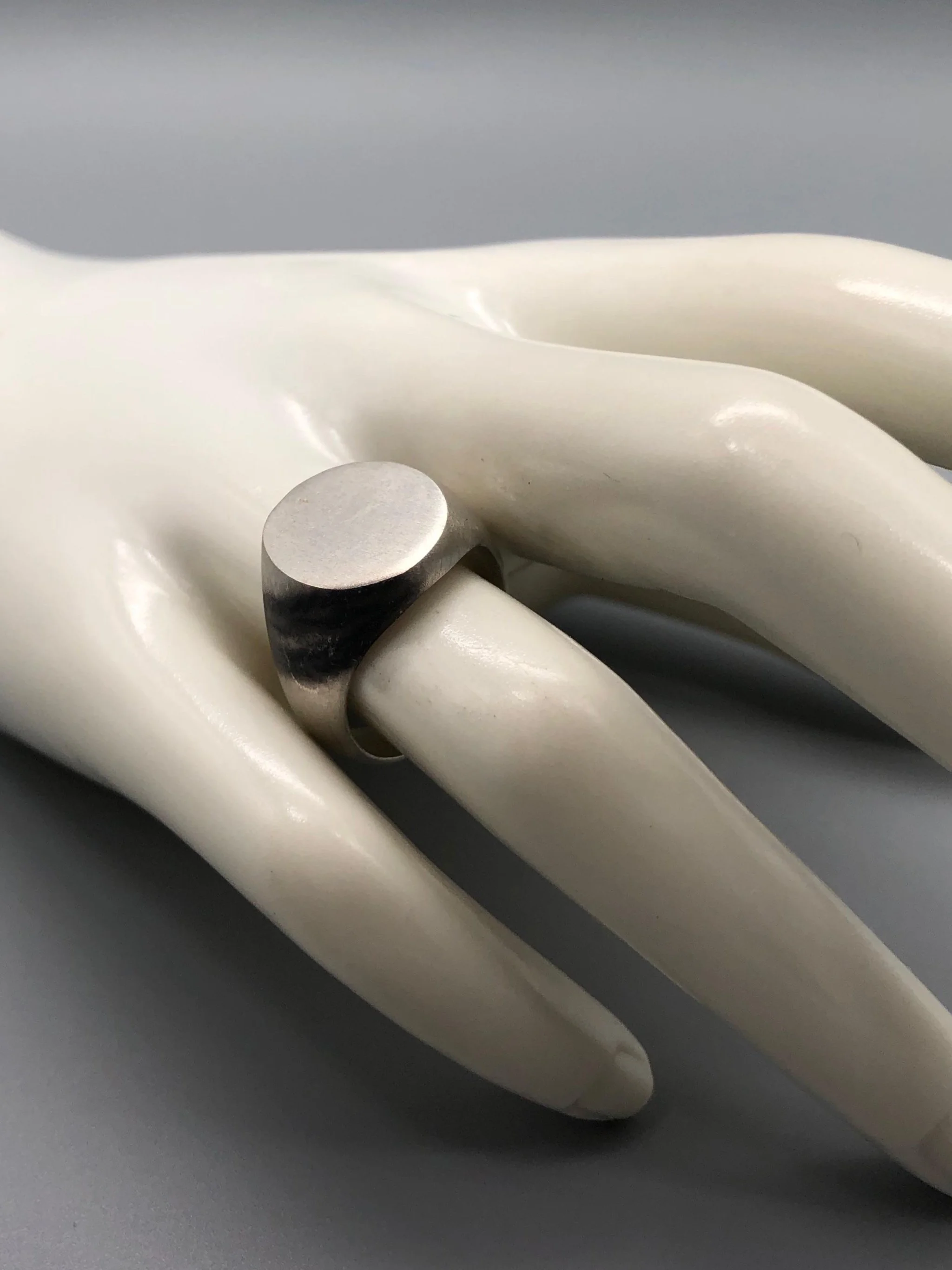 Anello Chevalière in argento opaco, gioiello contemporaneo dal volume pieno e dal design essenziale. Chevalière ring in matte silver, contemporary jewellery with a solid volume and essential design.