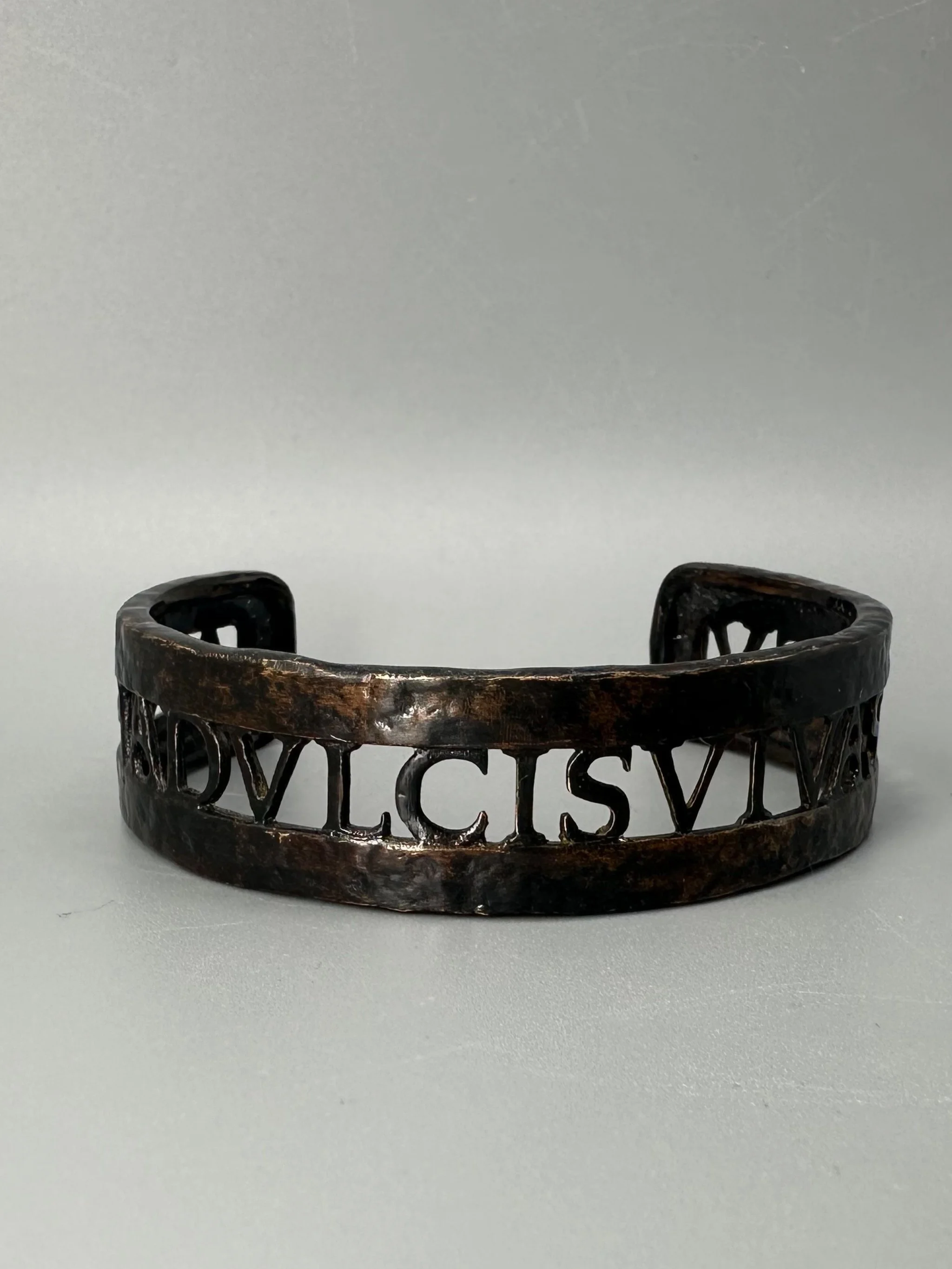 Bracciale Anima Dulcis di CōDICEDS in bronzo brunito, aperto e regolabile, con iscrizione latina traforata.  CōDICEDS Anima Dulcis open adjustable cuff in darkened bronze with openwork Latin inscripti