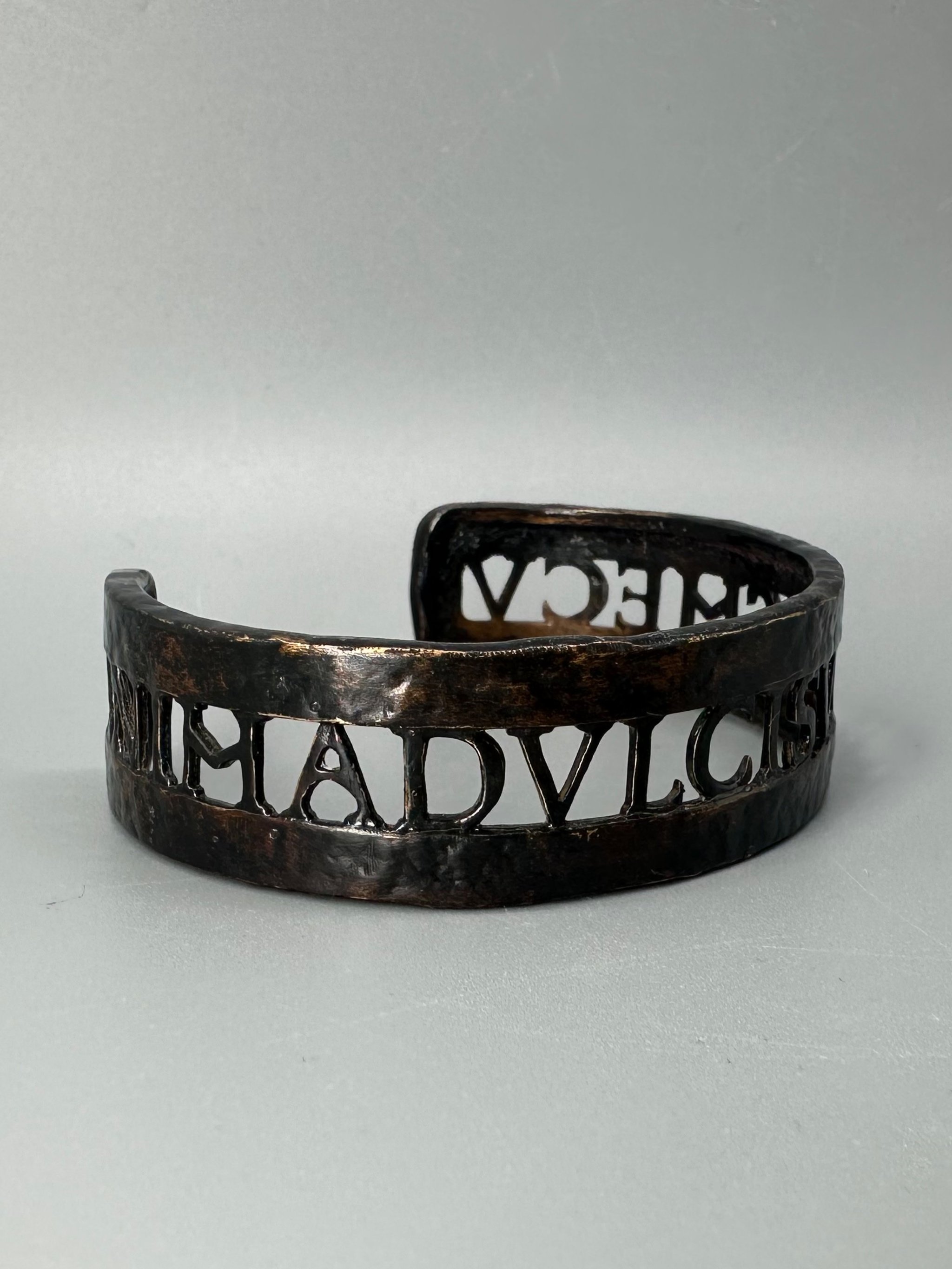 Bracciale Anima Dulcis di CōDICEDS in bronzo brunito, aperto e regolabile, con iscrizione latina traforata.  CōDICEDS Anima Dulcis open adjustable cuff in darkened bronze with openwork Latin inscripti