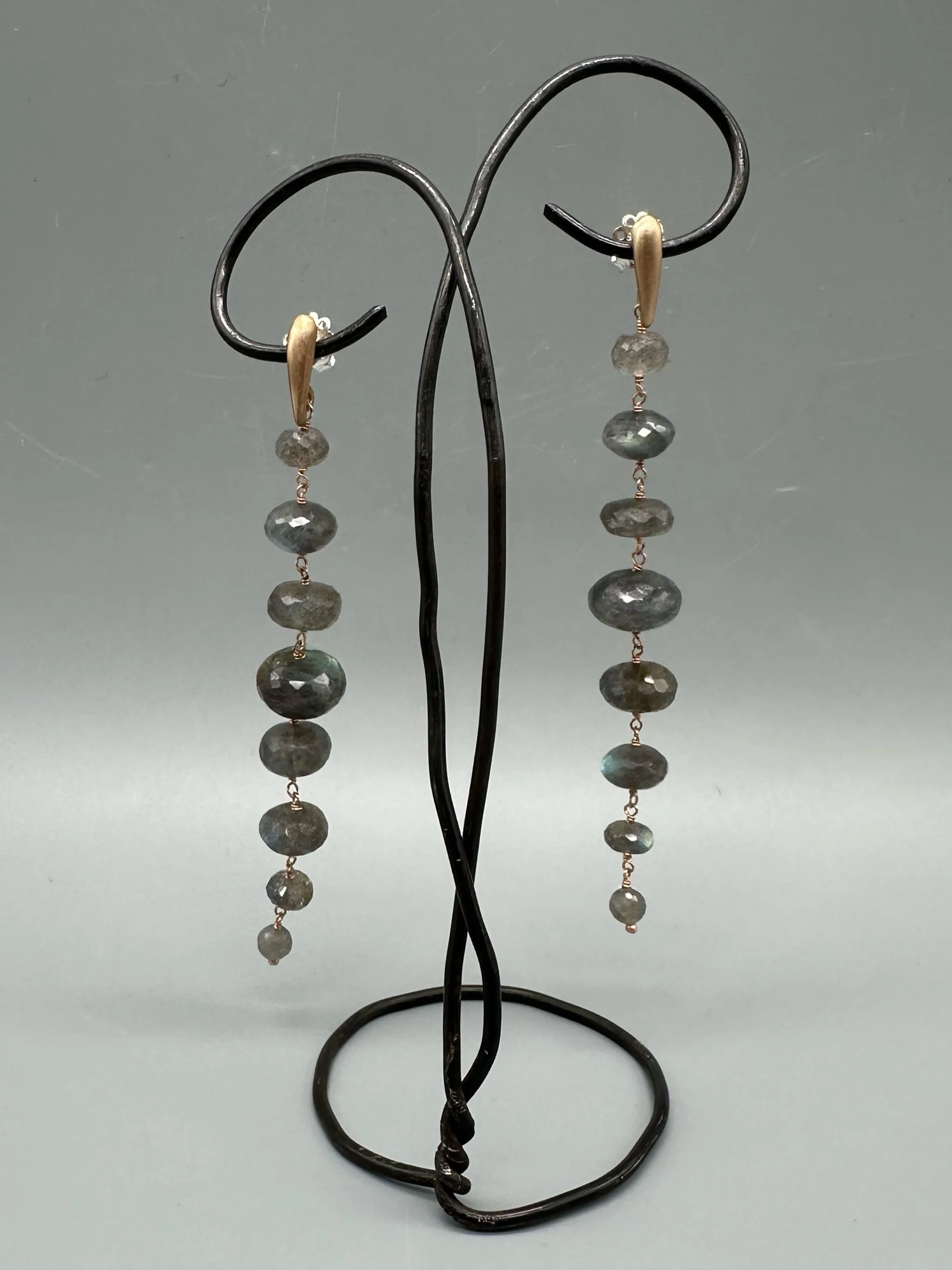 Orecchini Bold Labradorite con pietre grigie sfaccettate dai riflessi blu e verdi, disposte in verticale. Bold Labradorite earrings with vertically arranged faceted grey gemstones and blue-green refle