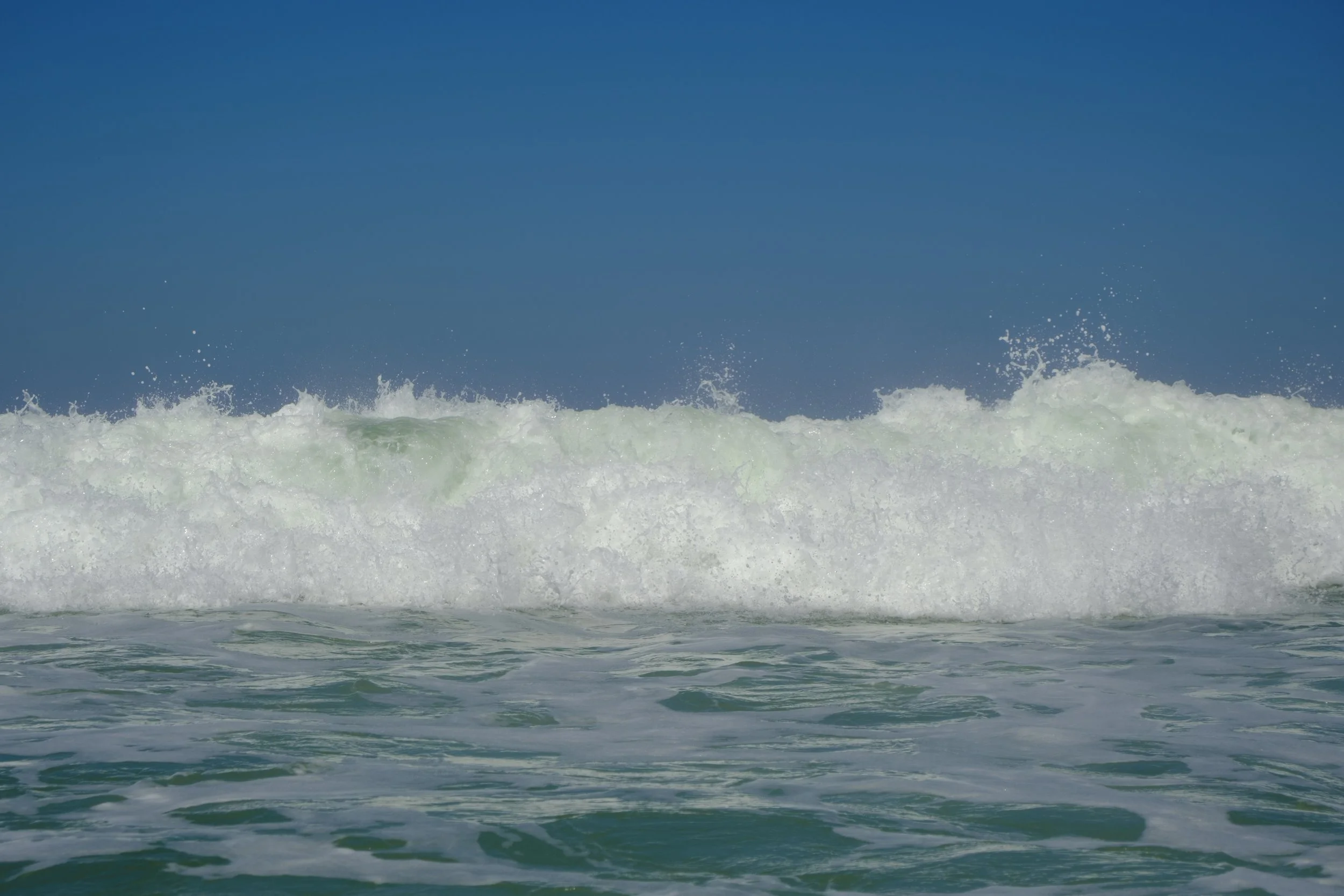 Ocean waves crashing under a clear blue sky.