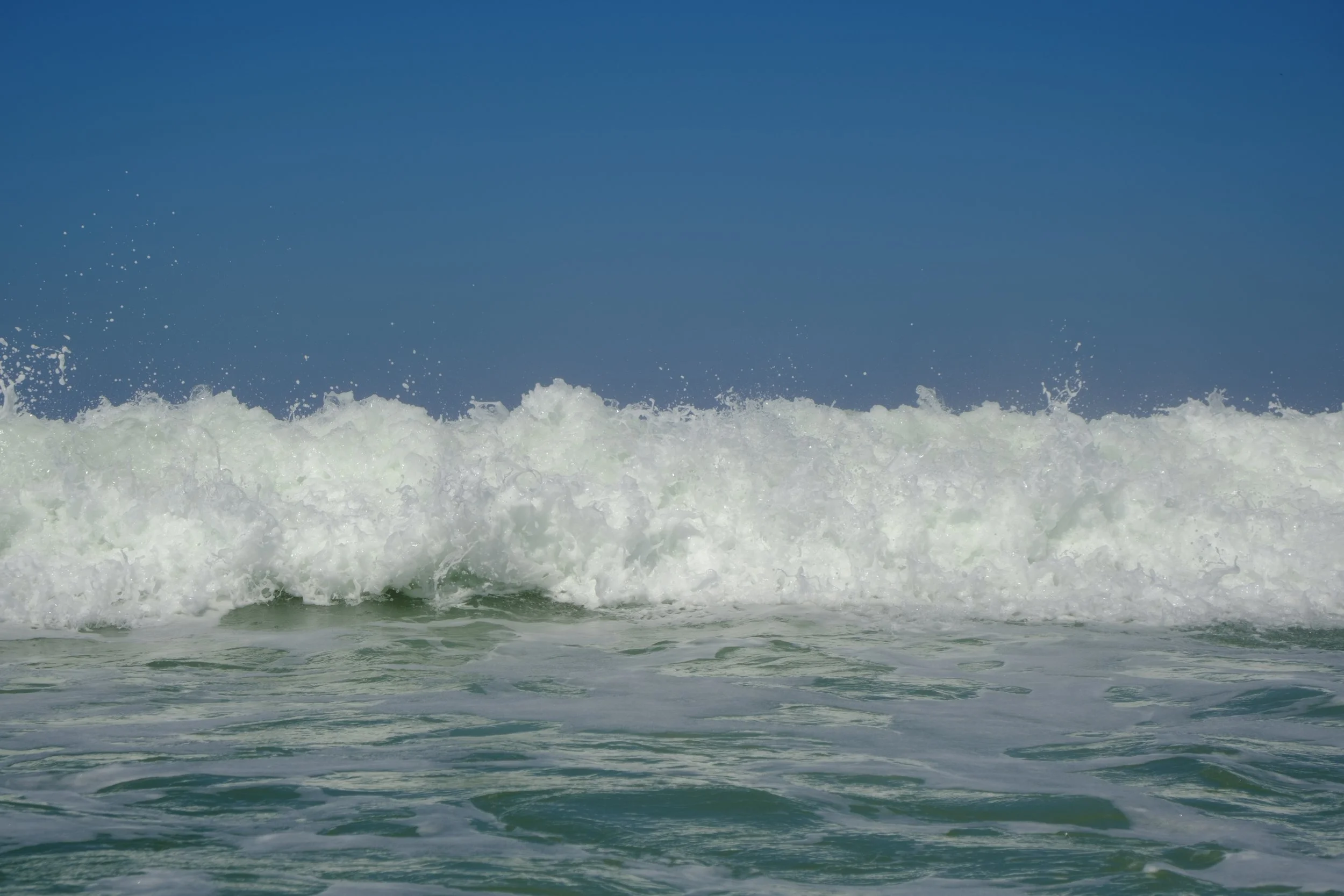 Ocean waves crashing under a clear blue sky.
