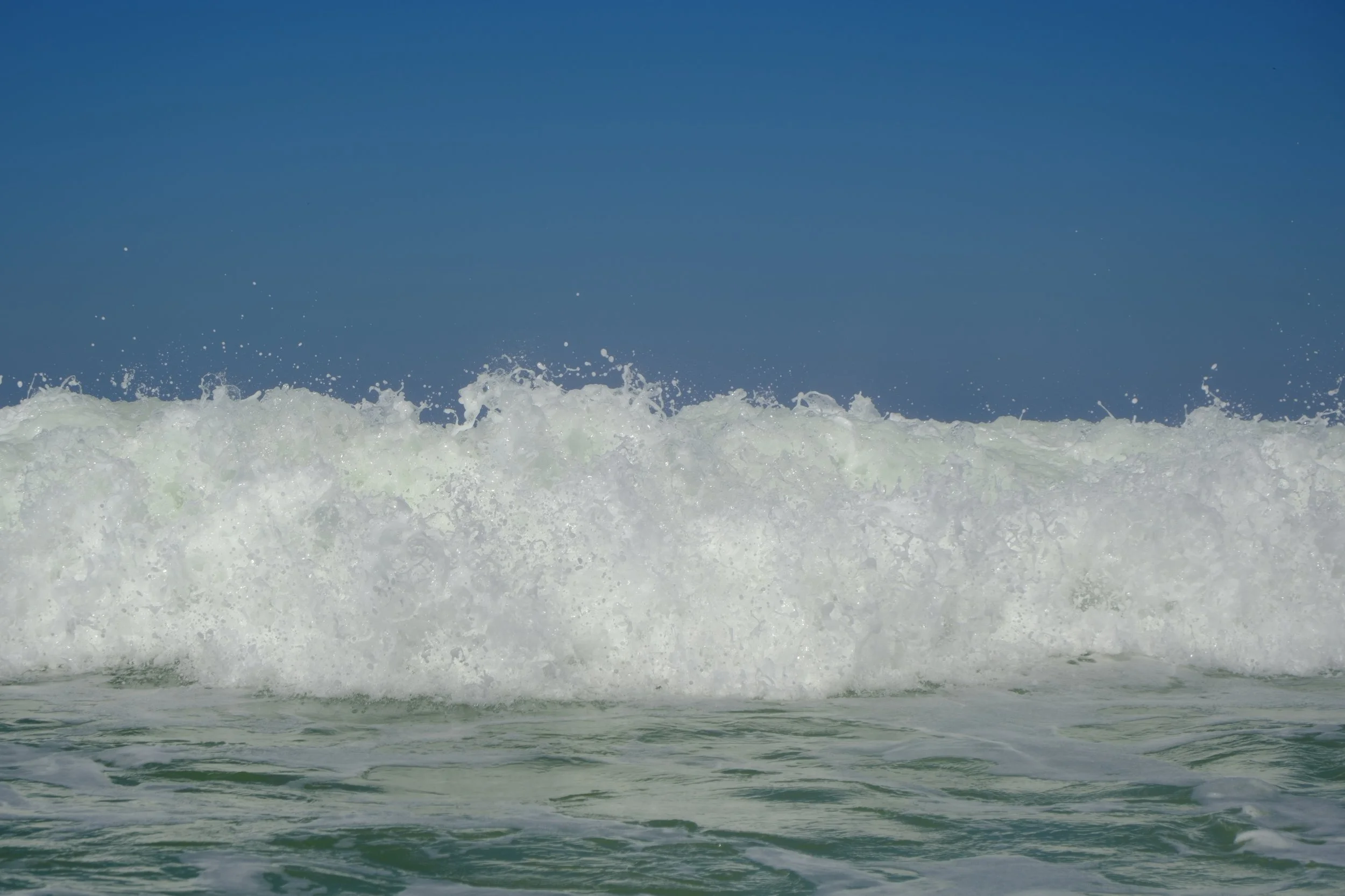 Waves crashing on the shore with a clear blue sky in the background.