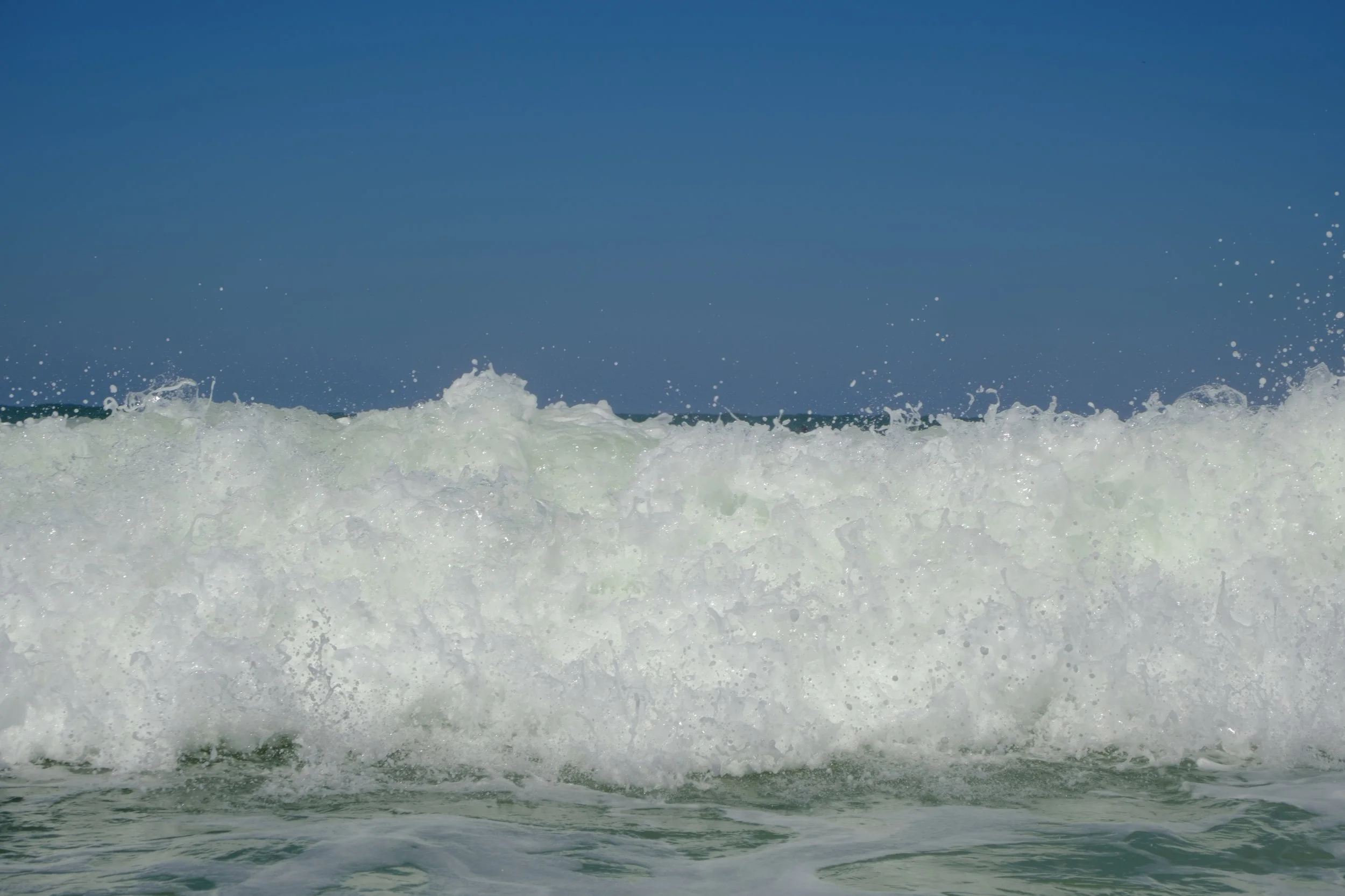 Waves crashing on the ocean under a clear blue sky.