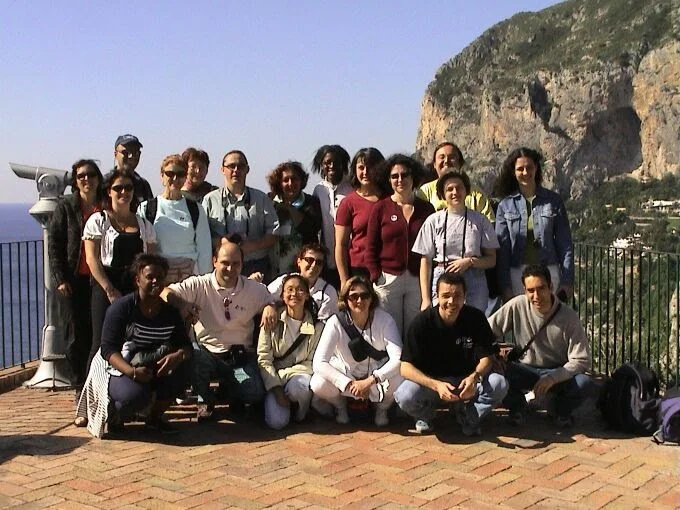 Group of people on a terrace with a mountain and coastline in the background.