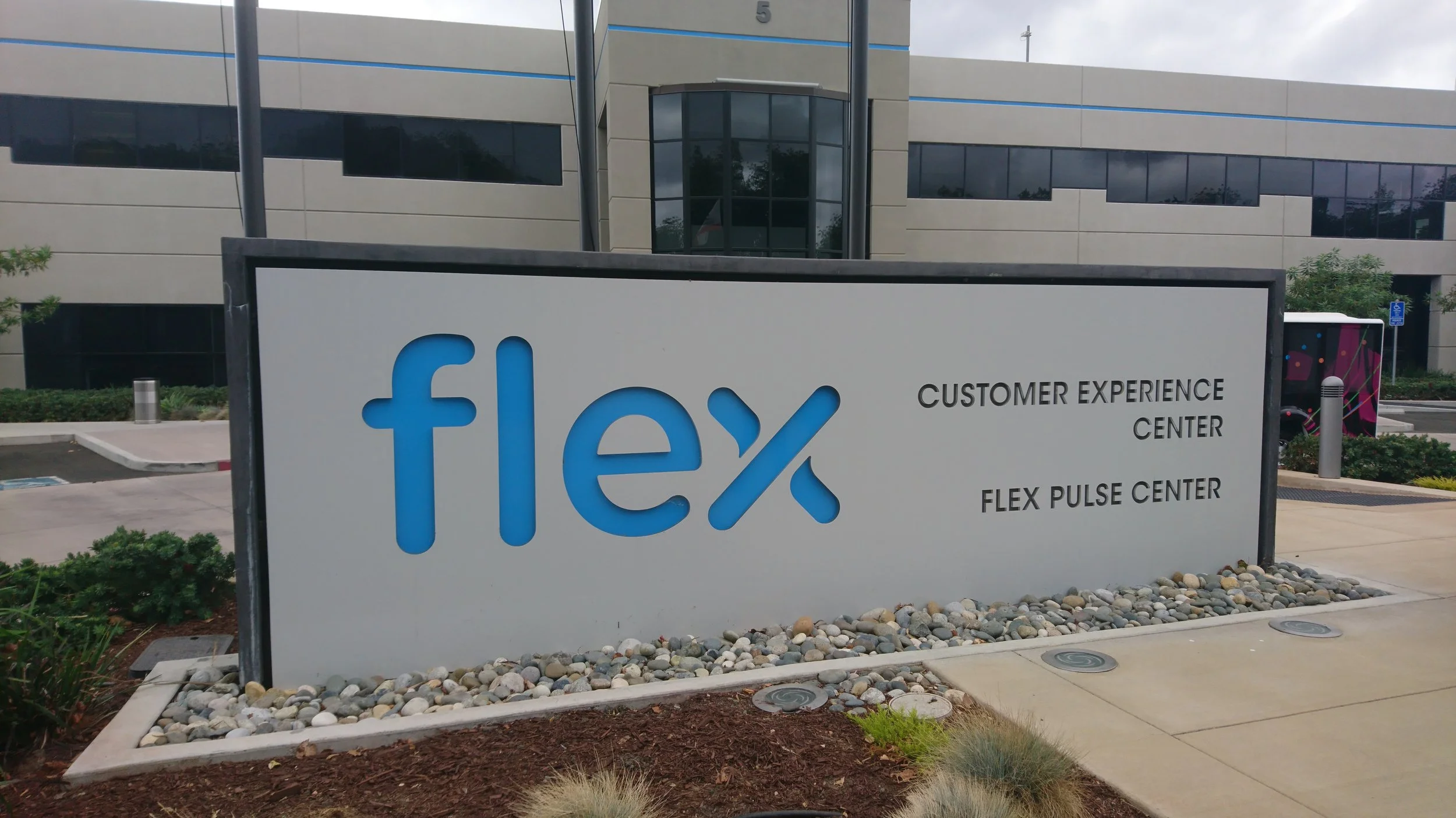Sign for the Flex company showing the logo 'flex' in blue and information about customer experience center and flex pulse center outside a modern building