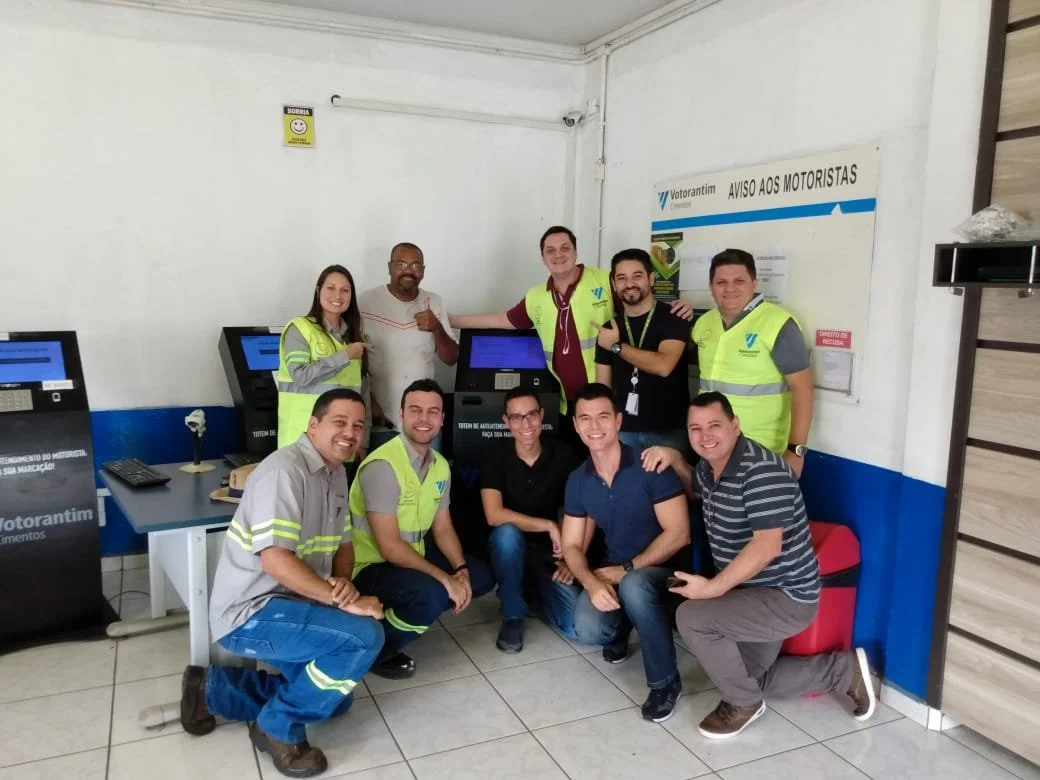 Group of people at a transportation office, some wearing safety vests, standing and kneeling in front of self-service kiosks